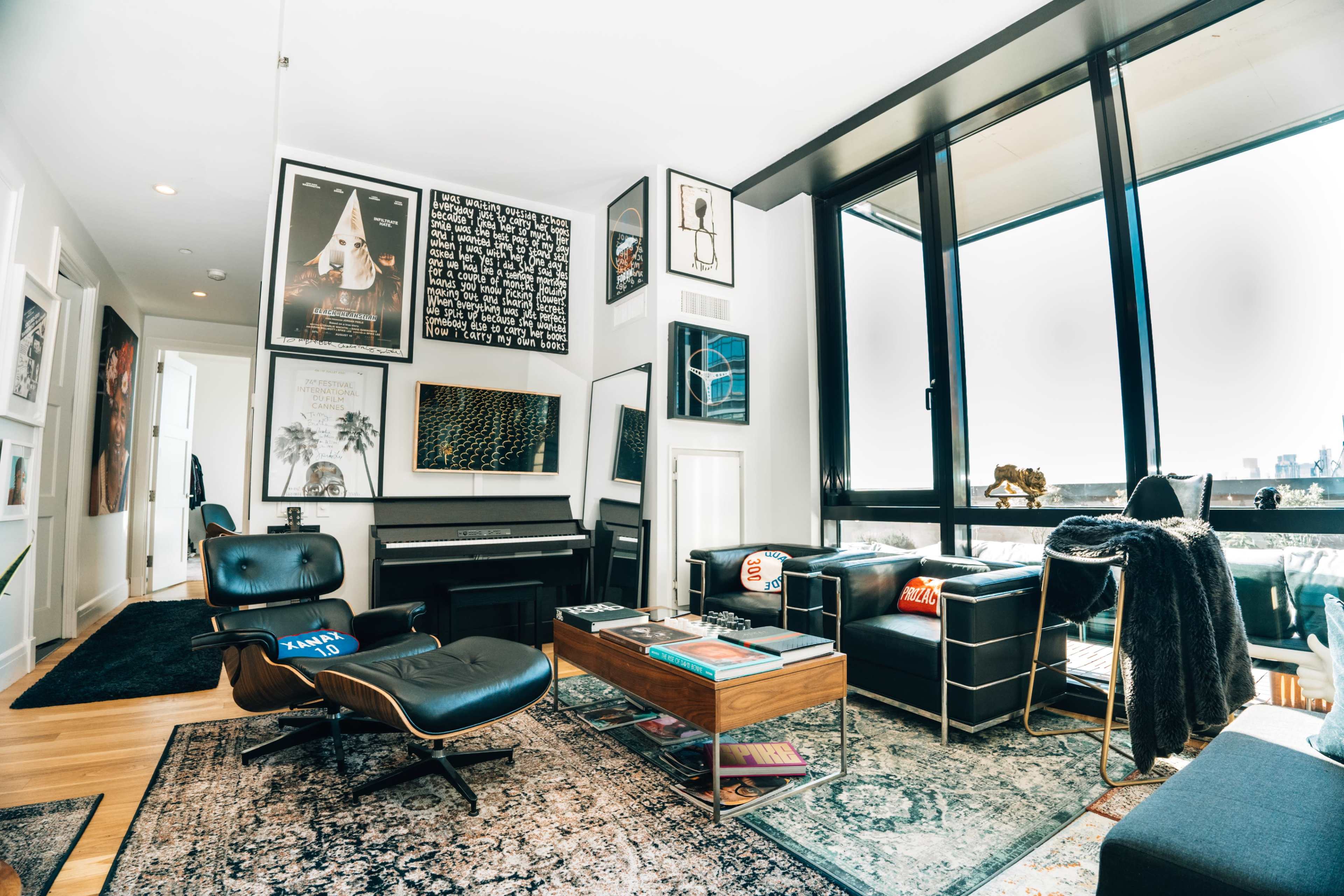 The image shows a modern living room featuring a piano, framed artwork on the walls, leather furniture, and a coffee table with books.