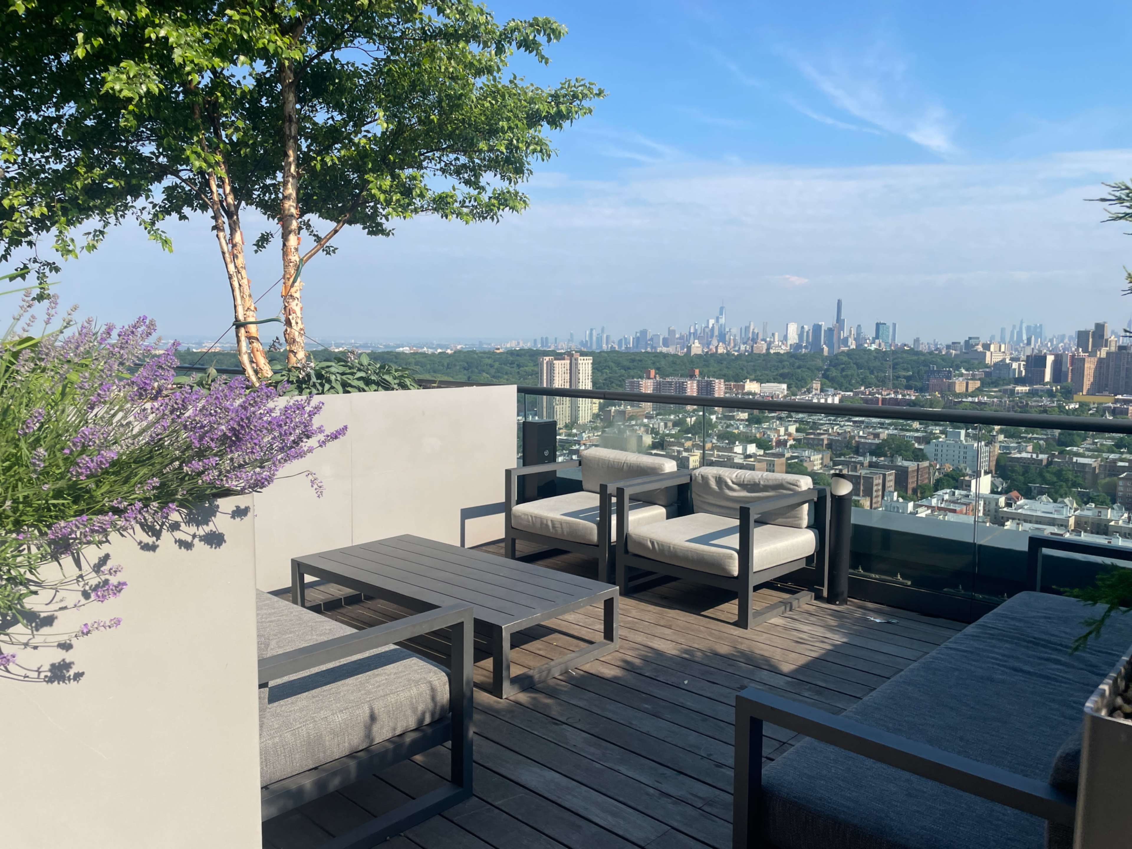 A rooftop patio features modern seating and a view of a city skyline against a clear blue sky.