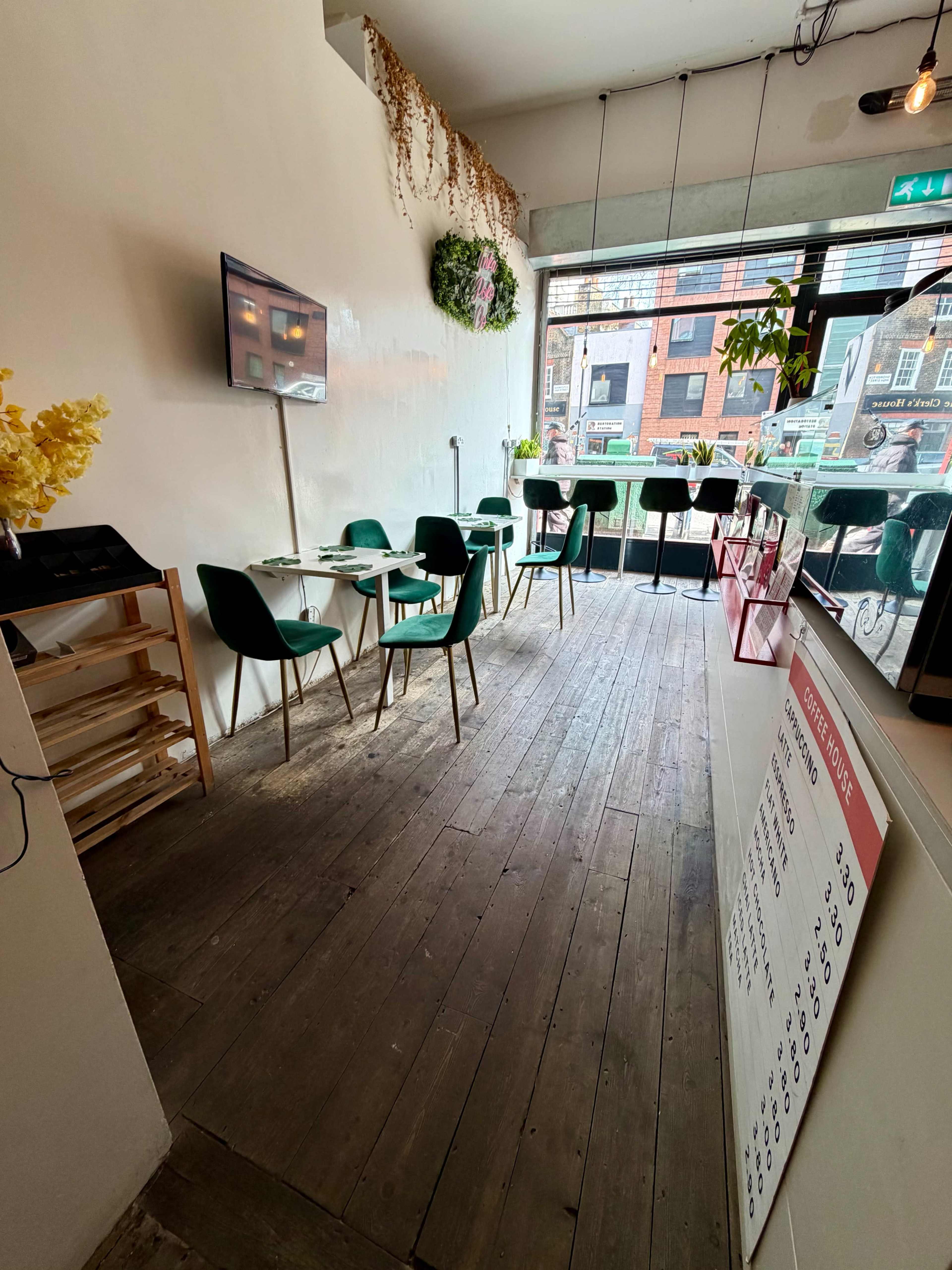 The image shows a modern café interior with green chairs and a white wall, featuring a menu board and a window view of the street outside.