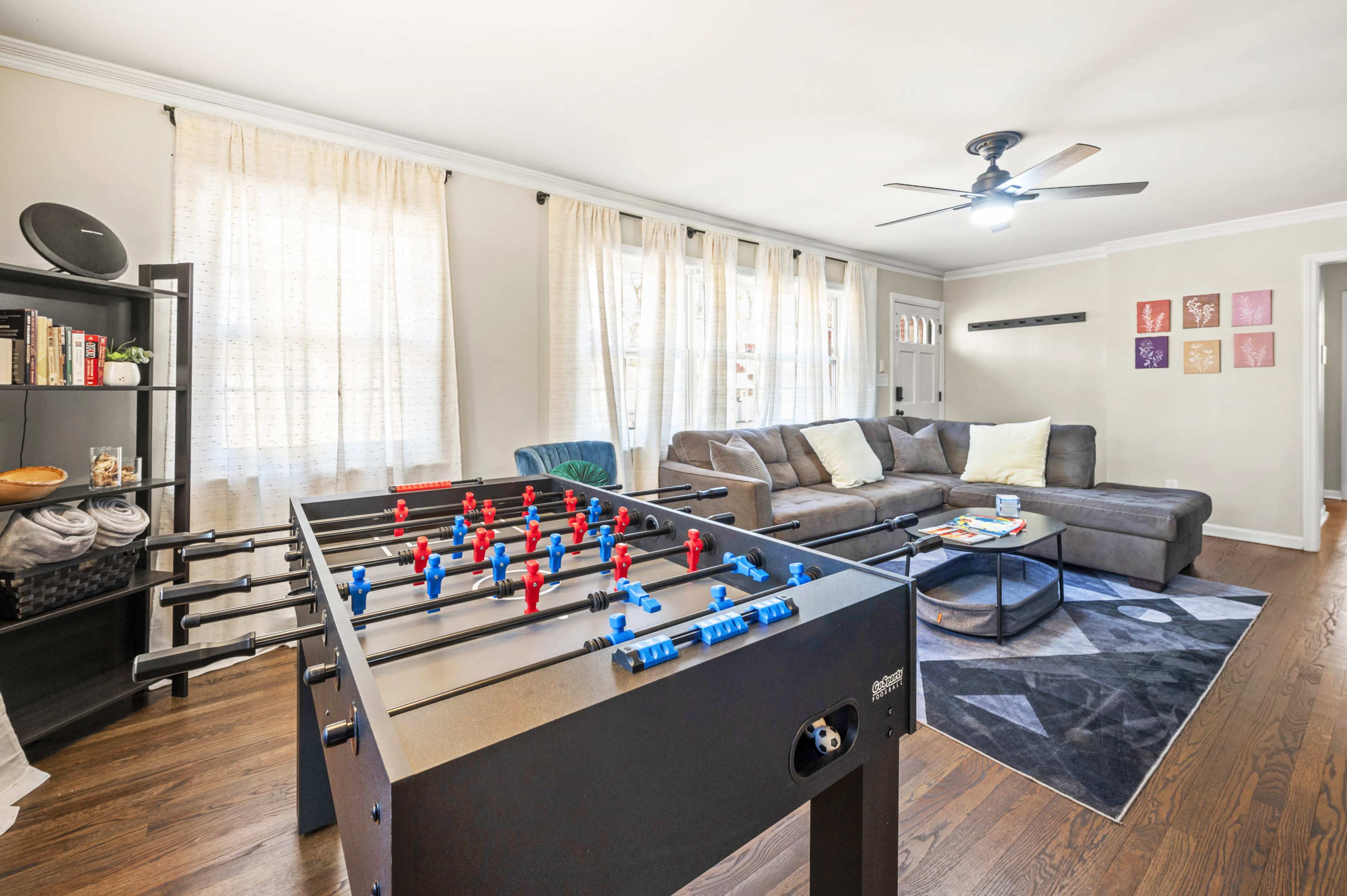 A foosball table is positioned in the foreground of a living room furnished with a couch, a coffee table, and book shelves.