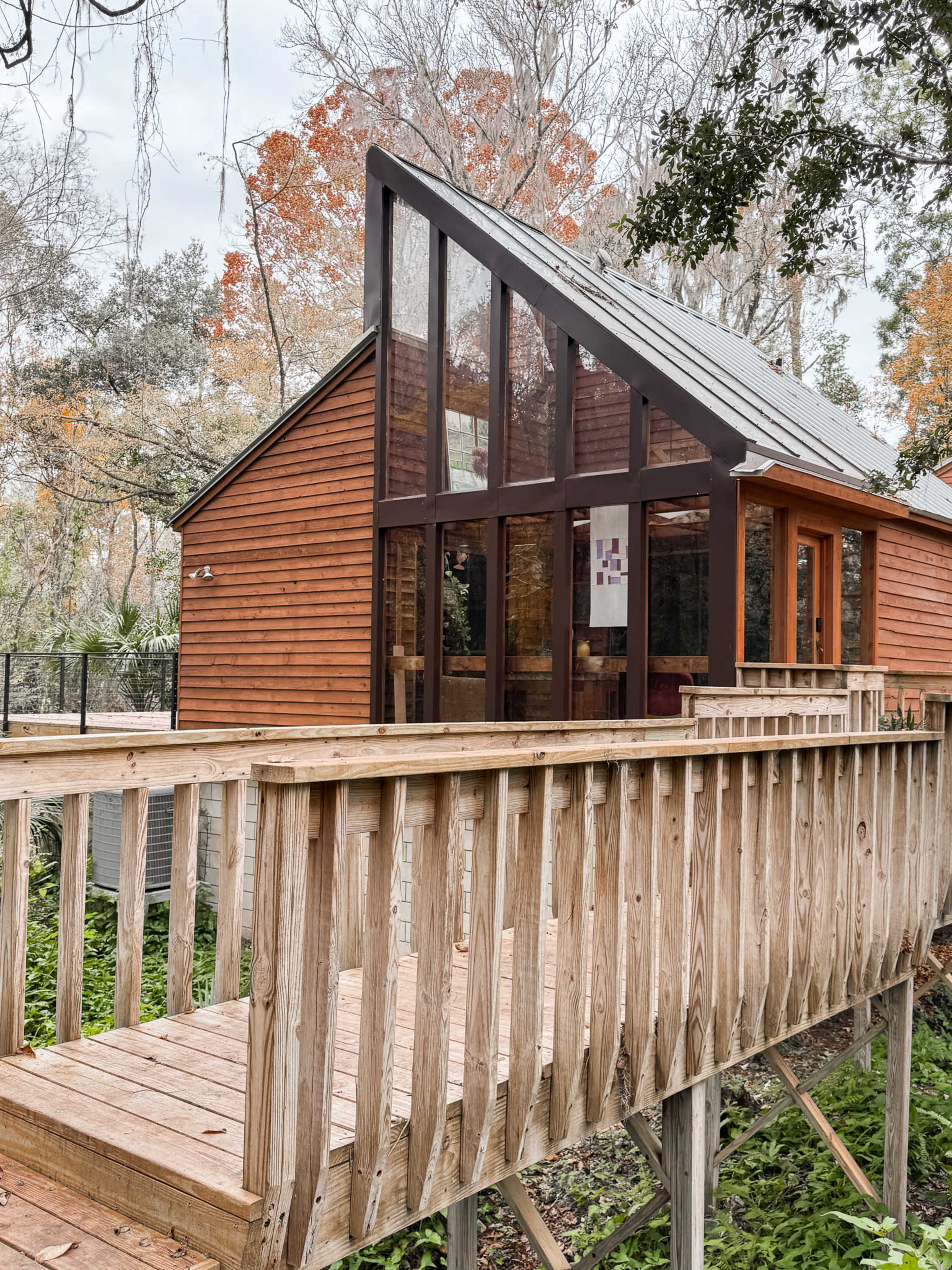 A wooden house with large windows and a slanted roof is positioned on stilts surrounded by trees.