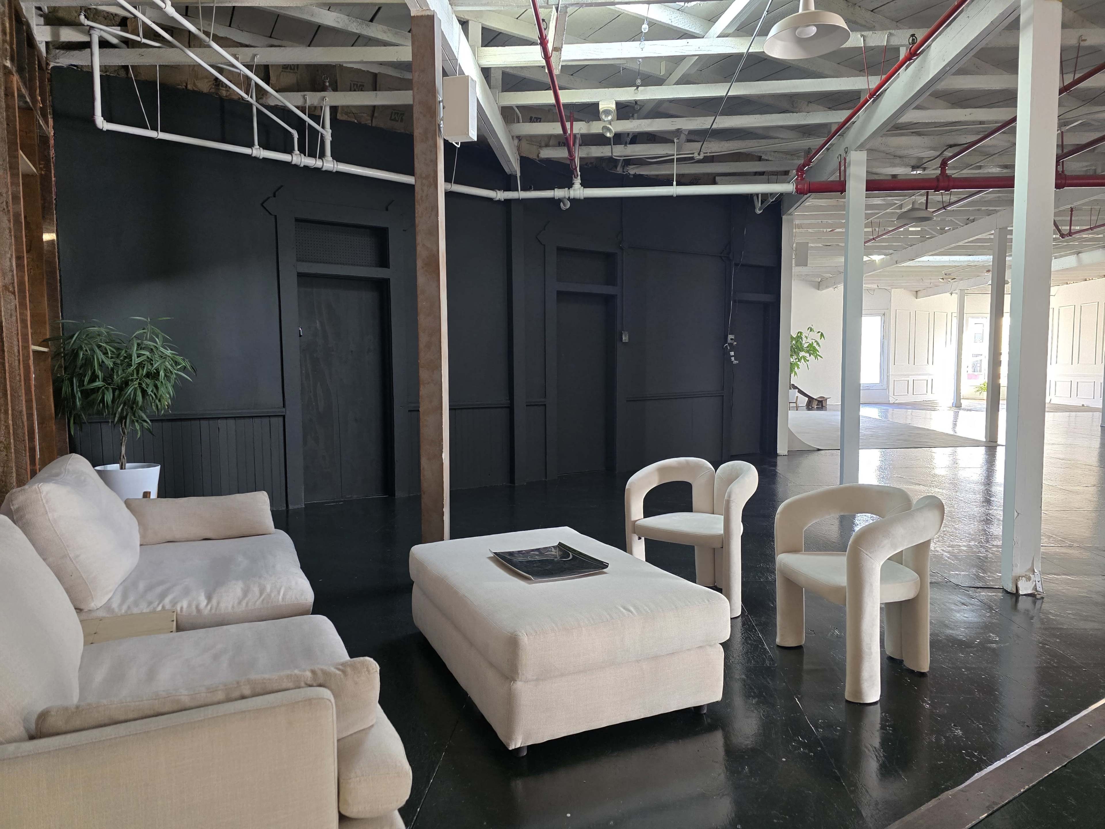 The image shows a spacious, modern interior with a light-colored sofa, two circular chairs, and a coffee table set against a dark wall.