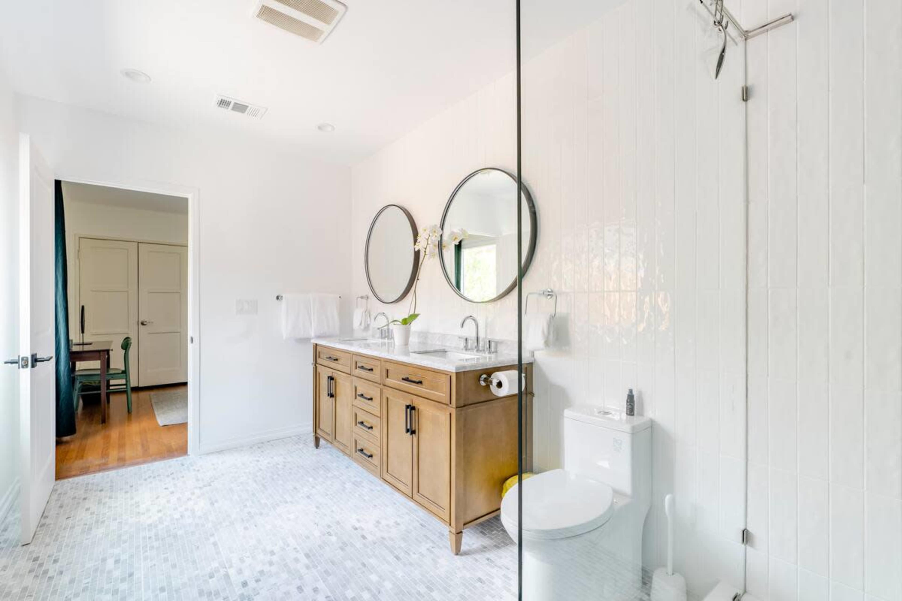 A modern bathroom with a double vanity, two round mirrors, a clear glass shower enclosure, and a white tiled floor.