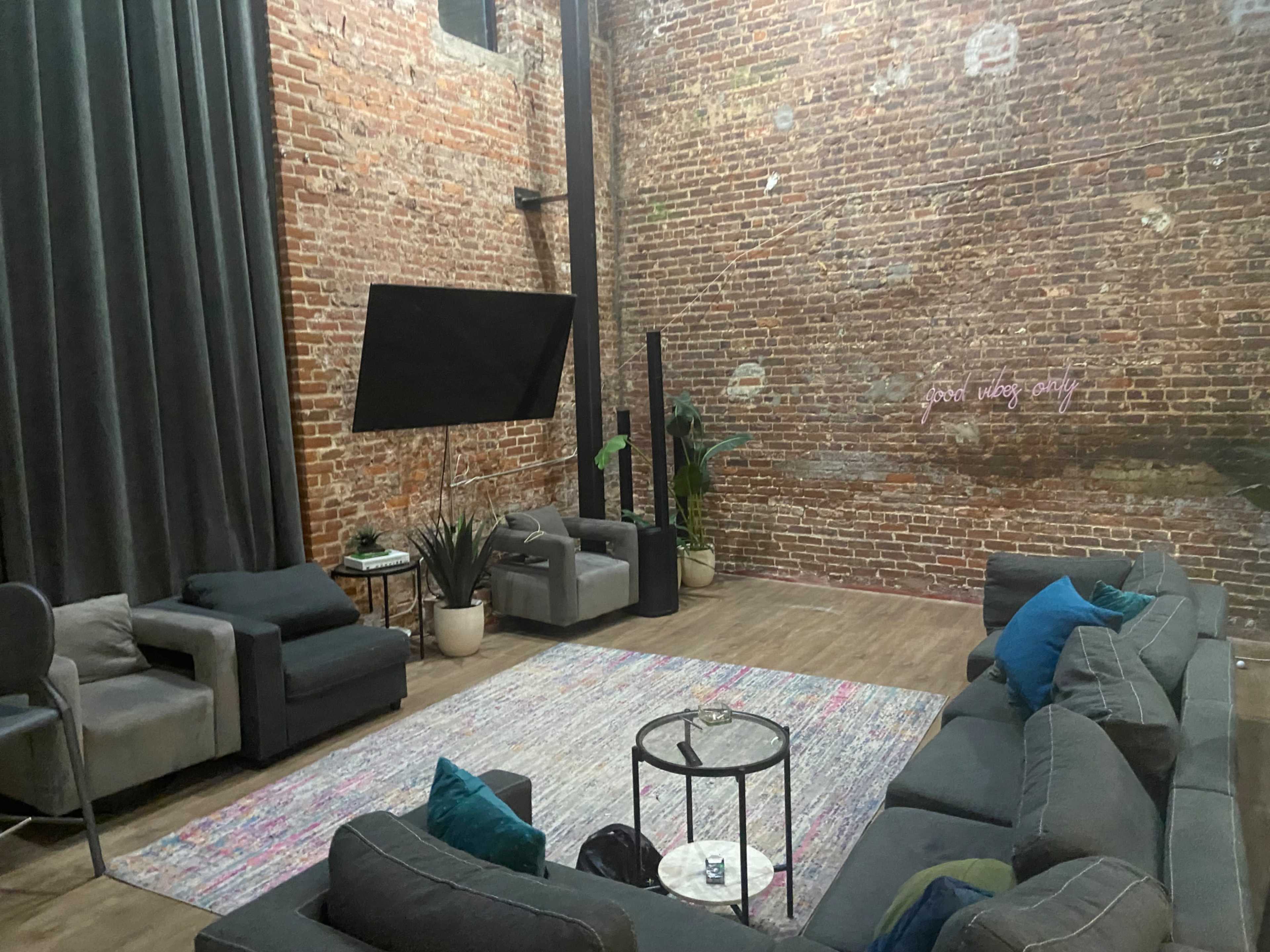 A spacious lounge area with exposed brick walls, a large rug, several seating options, and a mounted screen.