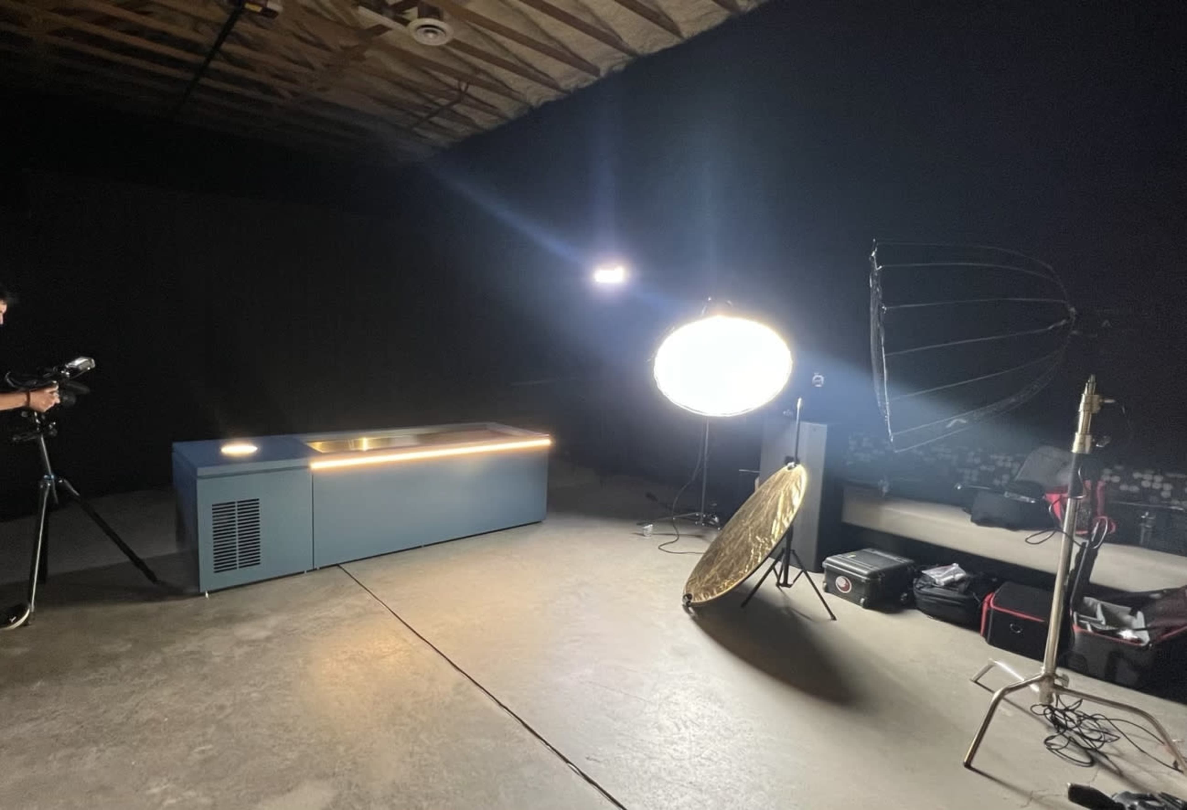 A photography setup features a blue table, studio lights, and camera equipment in a darkened space.