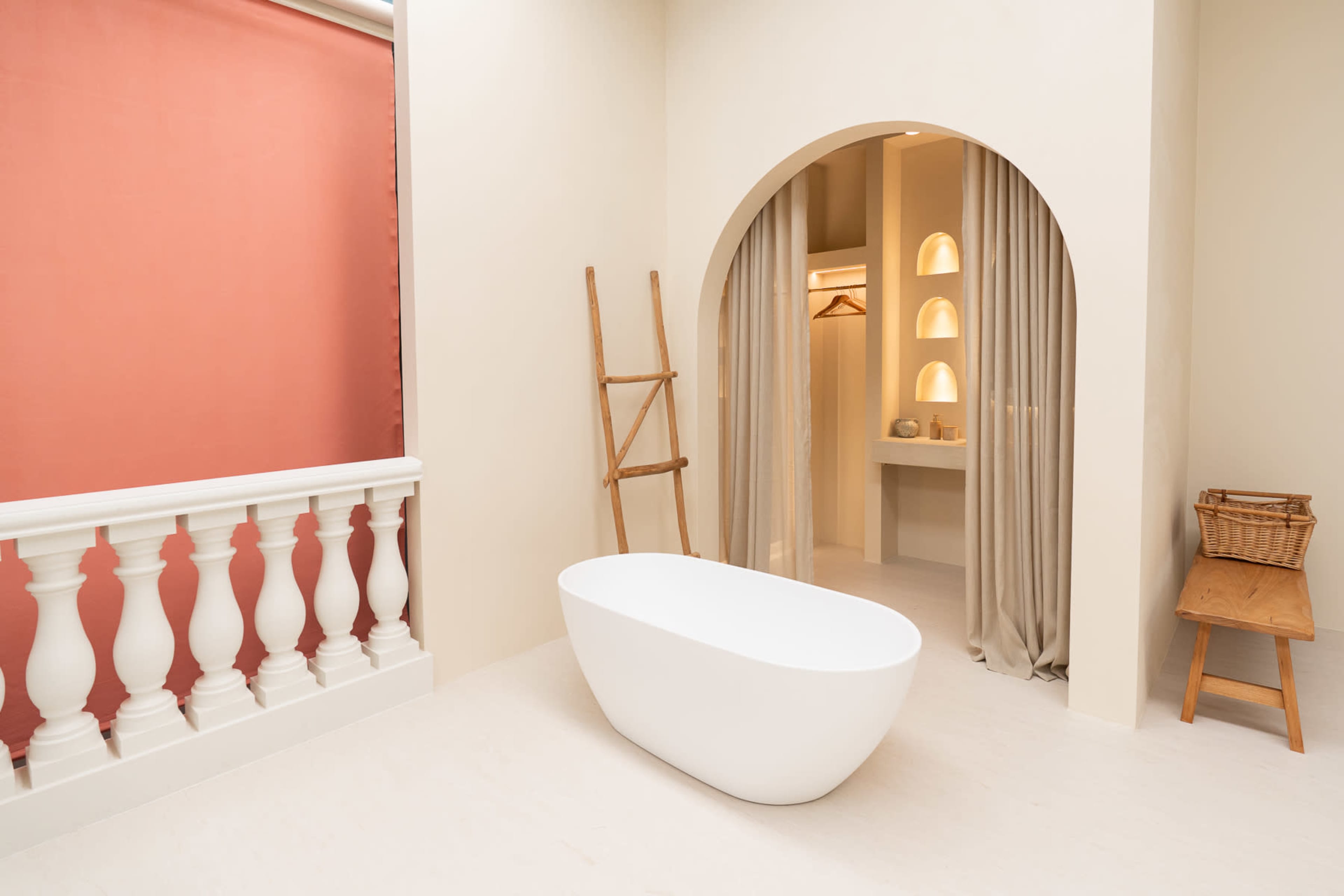 The image features a modern bathroom with a freestanding white bathtub, arched openings, and light-colored walls, complemented by a wooden ladder and simple furnishings.