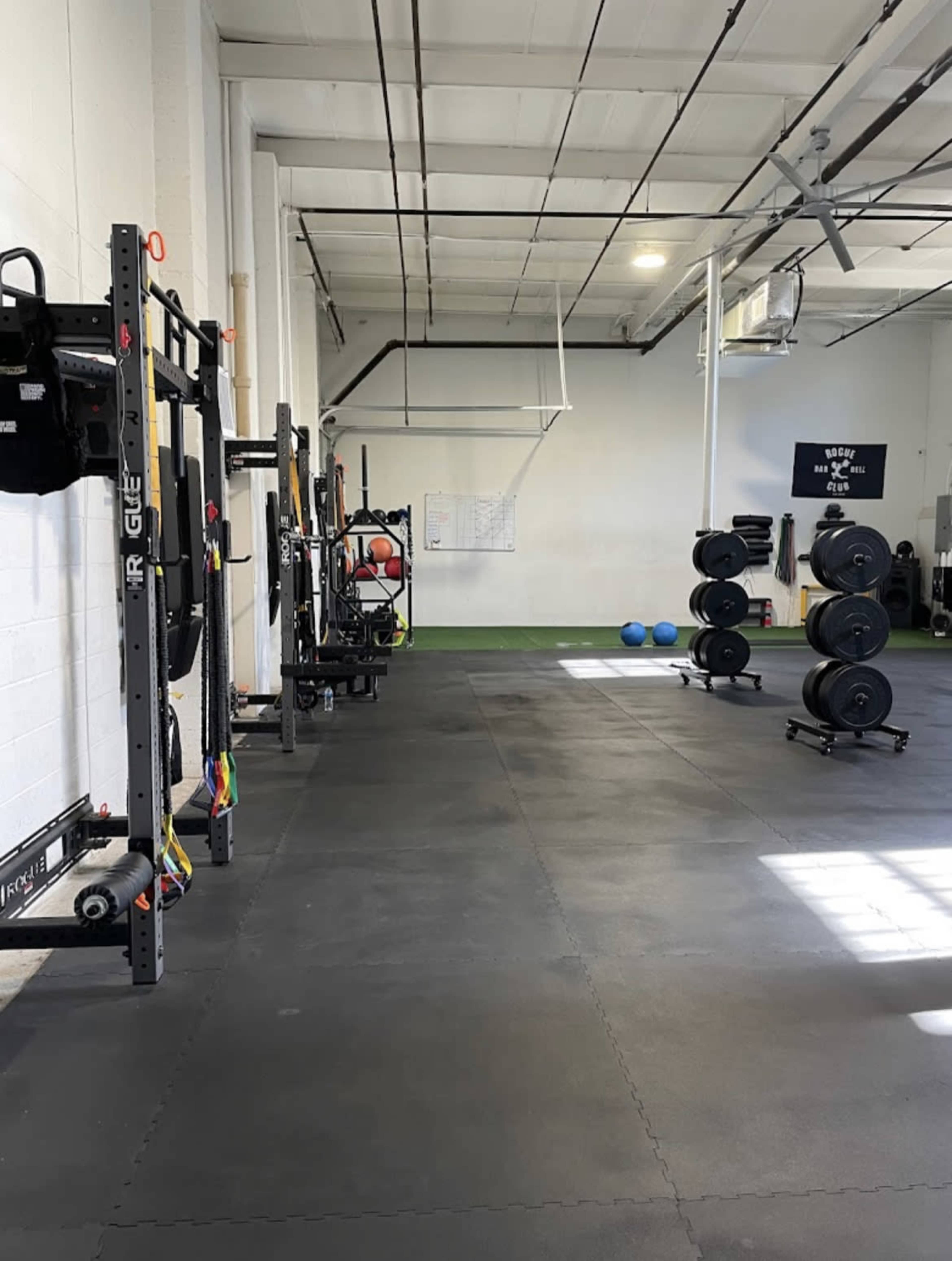 A spacious gym interior with weightlifting equipment, a squat rack, and various exercise mats arranged on a rubber floor.