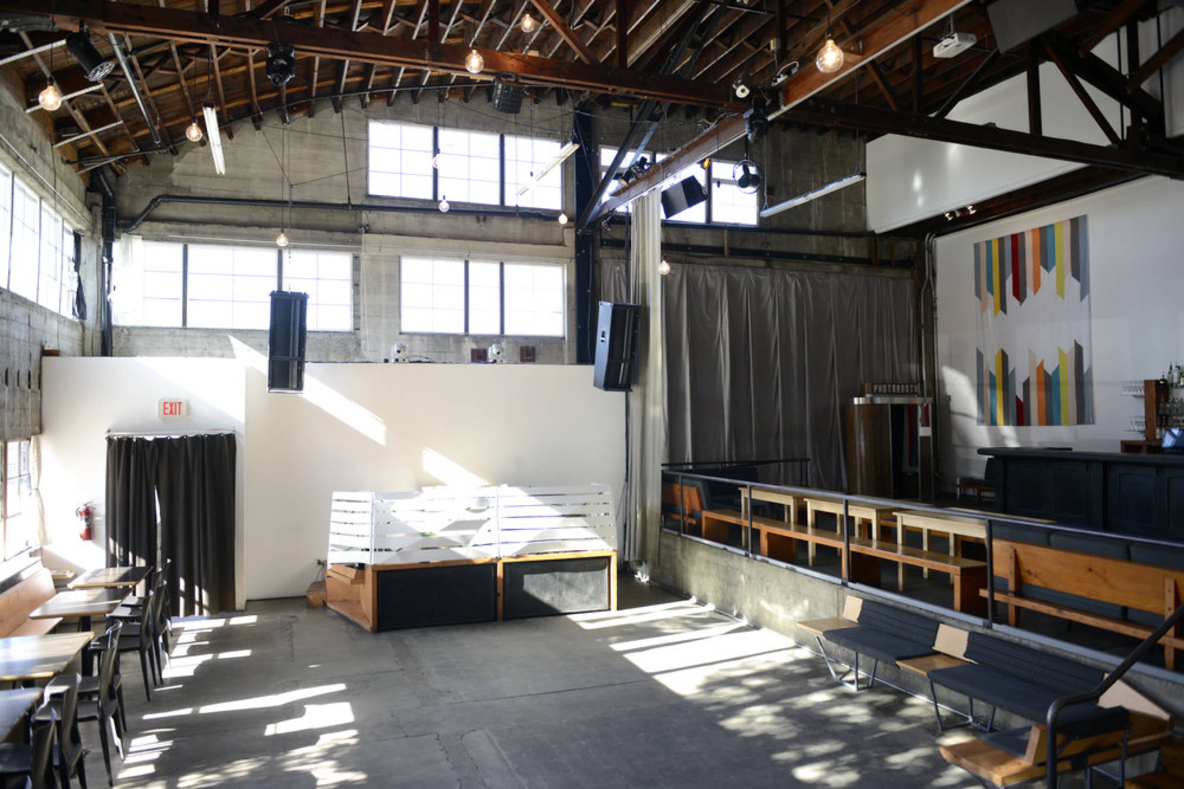 An interior space with high ceilings, large windows, wooden beams, and a combination of seating areas and a stage or performance space.