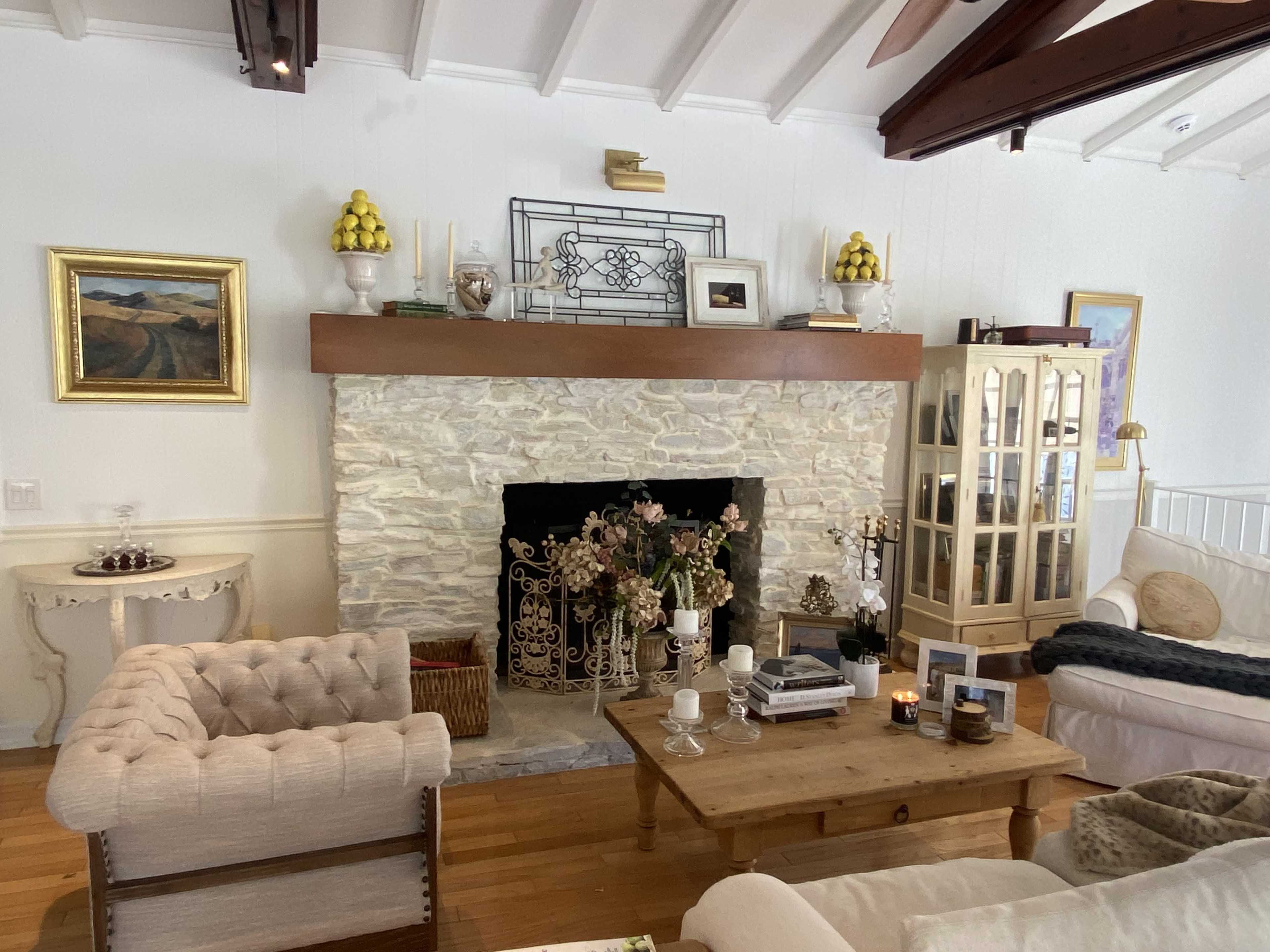 A cozy living room with a stone fireplace, wooden beams, and a mix of elegant and casual furniture.