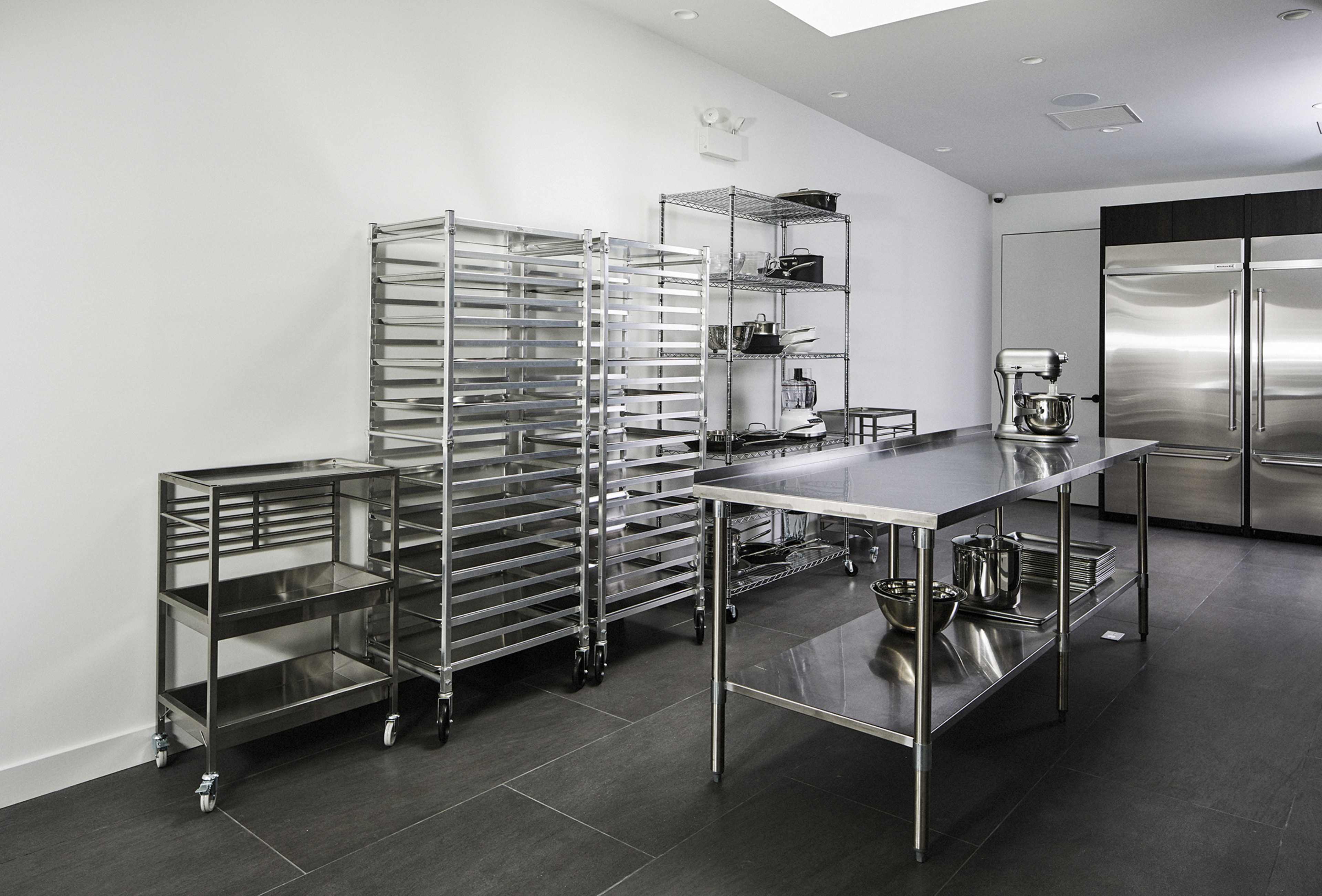 A modern kitchen with stainless steel shelving units, worktables, and a large refrigerator.