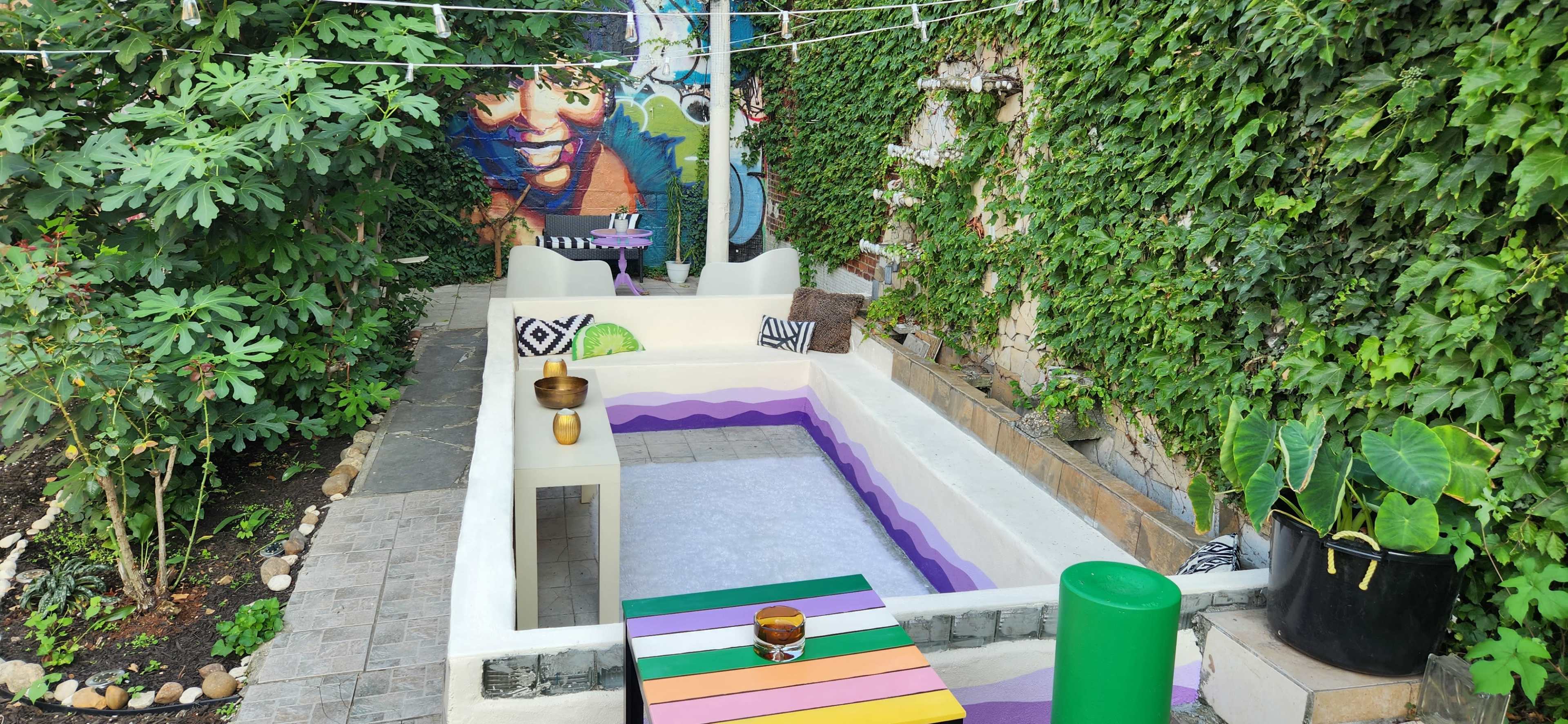 The image shows a creatively designed outdoor seating area with colorful benches, a mural on the wall, and greenery surrounding the space.