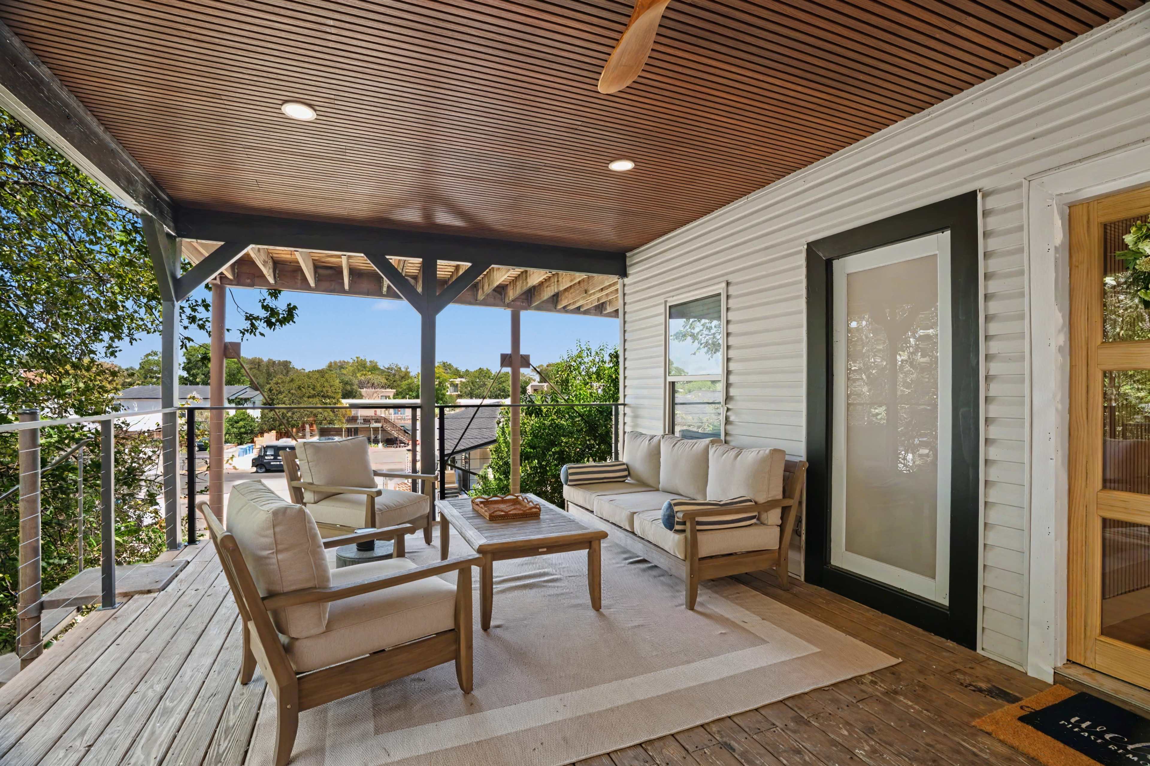 The image shows a cozy outdoor seating area with a wooden deck, featuring a couch, two armchairs, and a coffee table under a slatted ceiling.