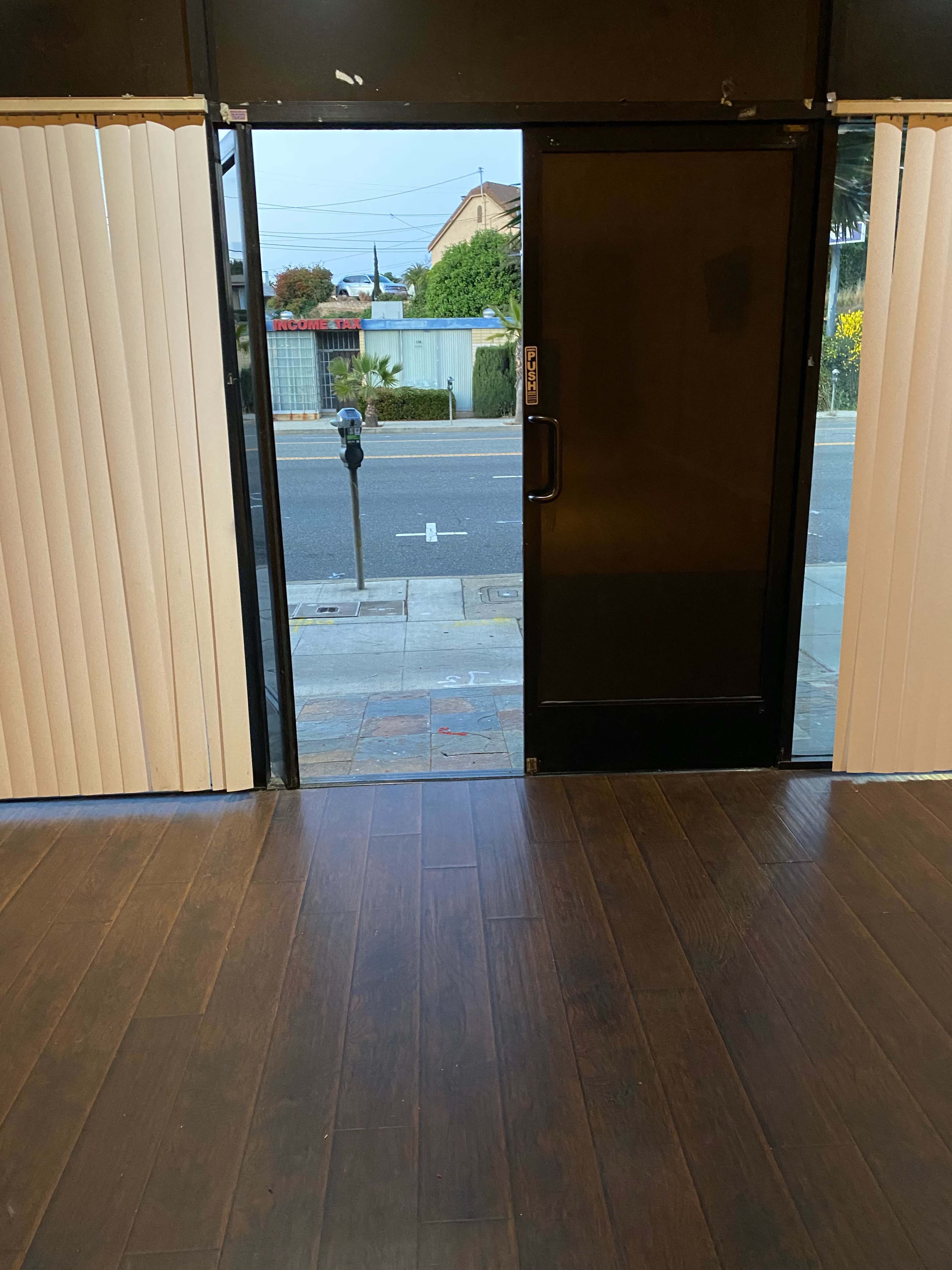 The image shows an open entrance with a glass door leading to a sidewalk and a parking meter outside.