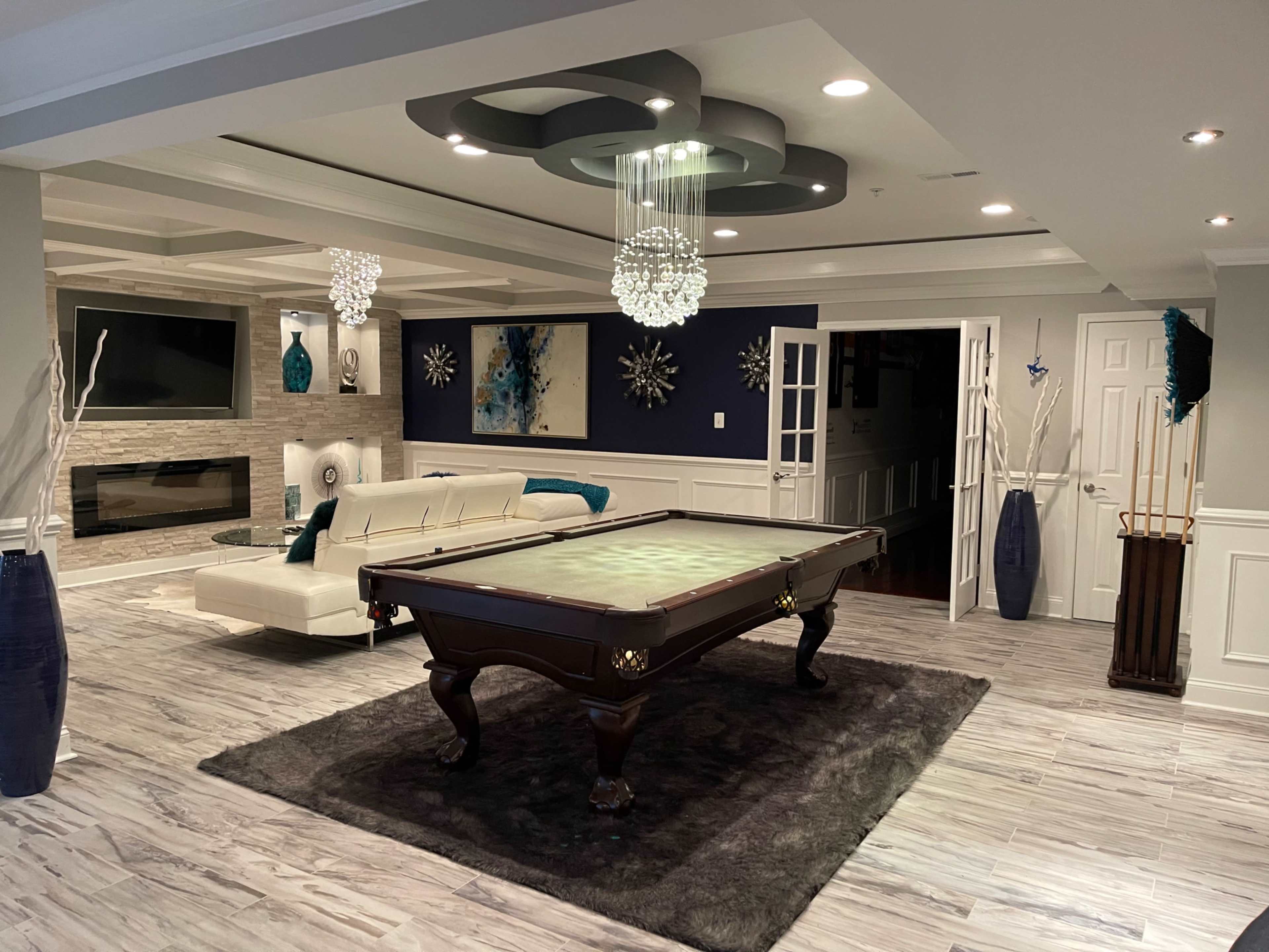 A spacious, modern game room featuring a billiard table at center, surrounded by stylish decor, including a sectional sofa and decorative vases.