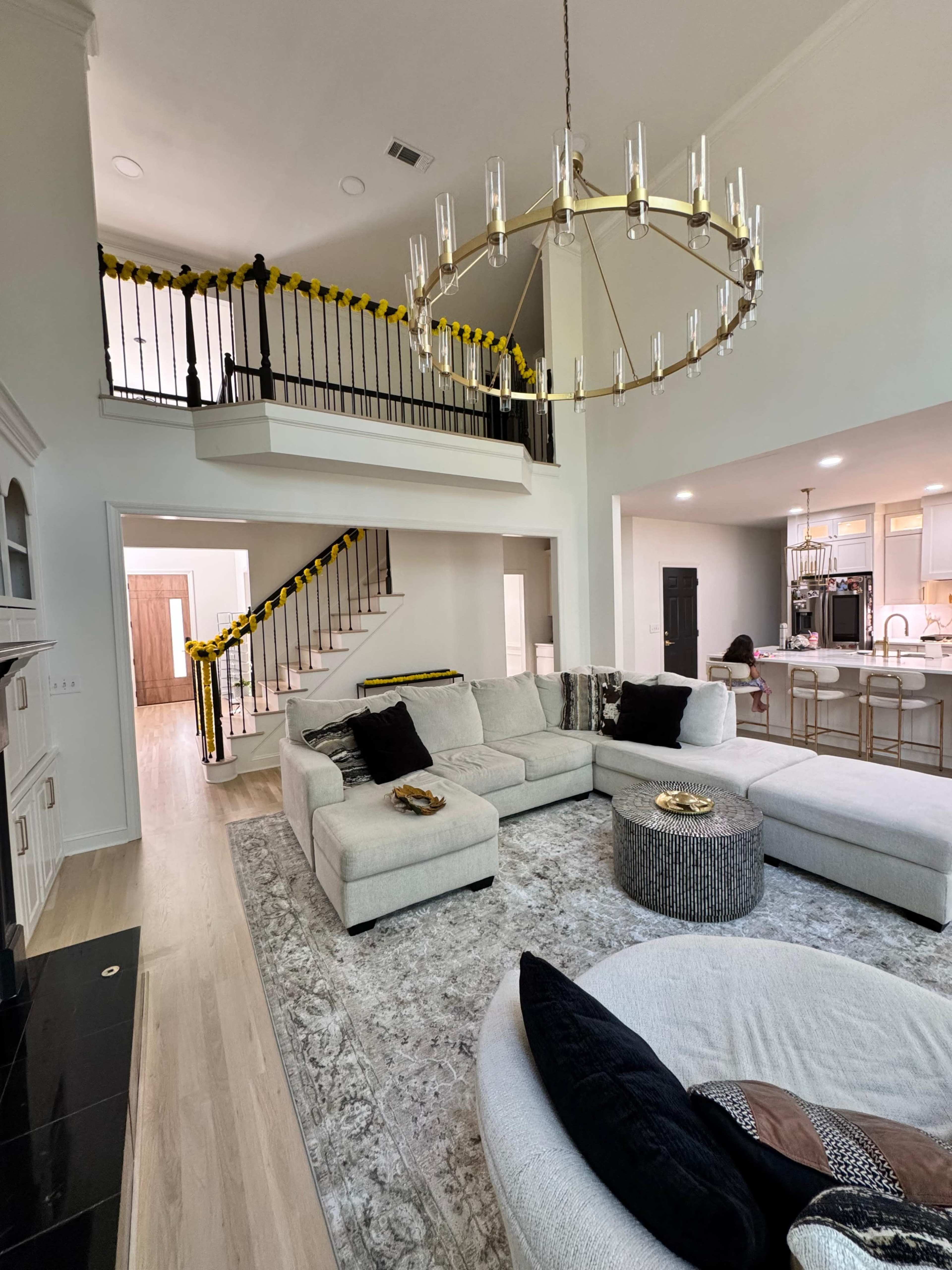 A spacious, modern living room with a large sectional sofa, a round coffee table, a chandelier, and a view of a staircase leading to a second floor.