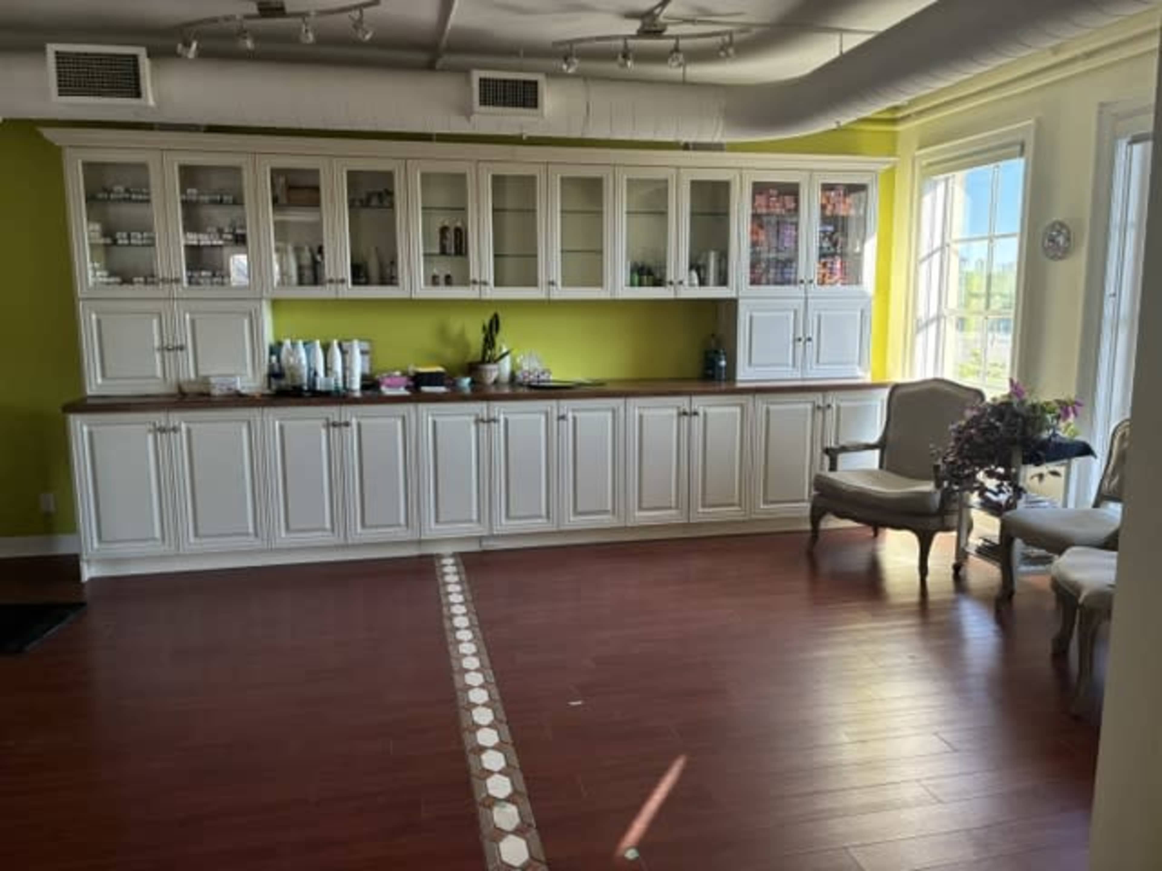 The image shows a well-organized room with a white cabinetry along a green wall, featuring a counter with various items, and two upholstered chairs in the corner.
