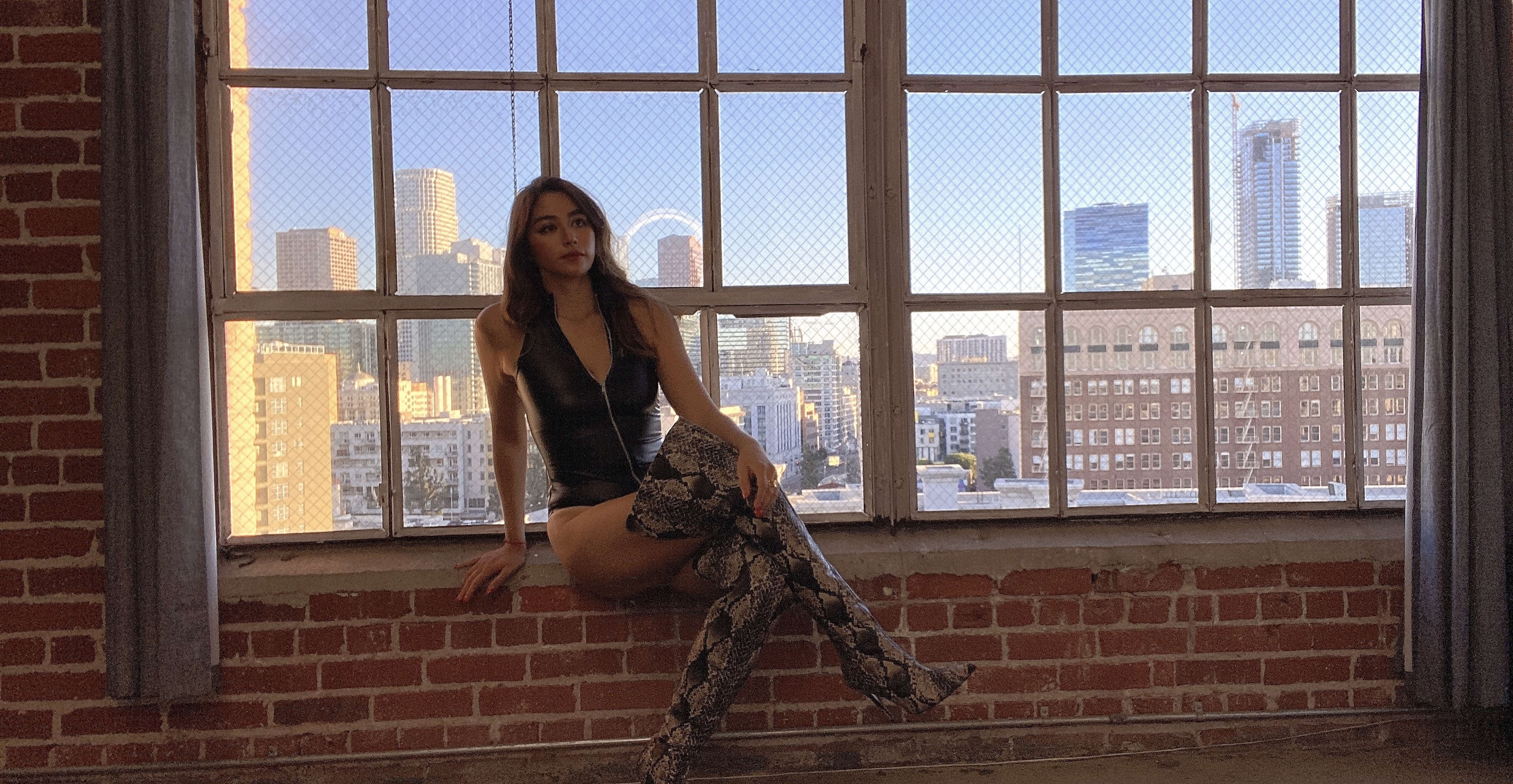 A model with tall boots posing on a window sill for a fashion photoshoot.