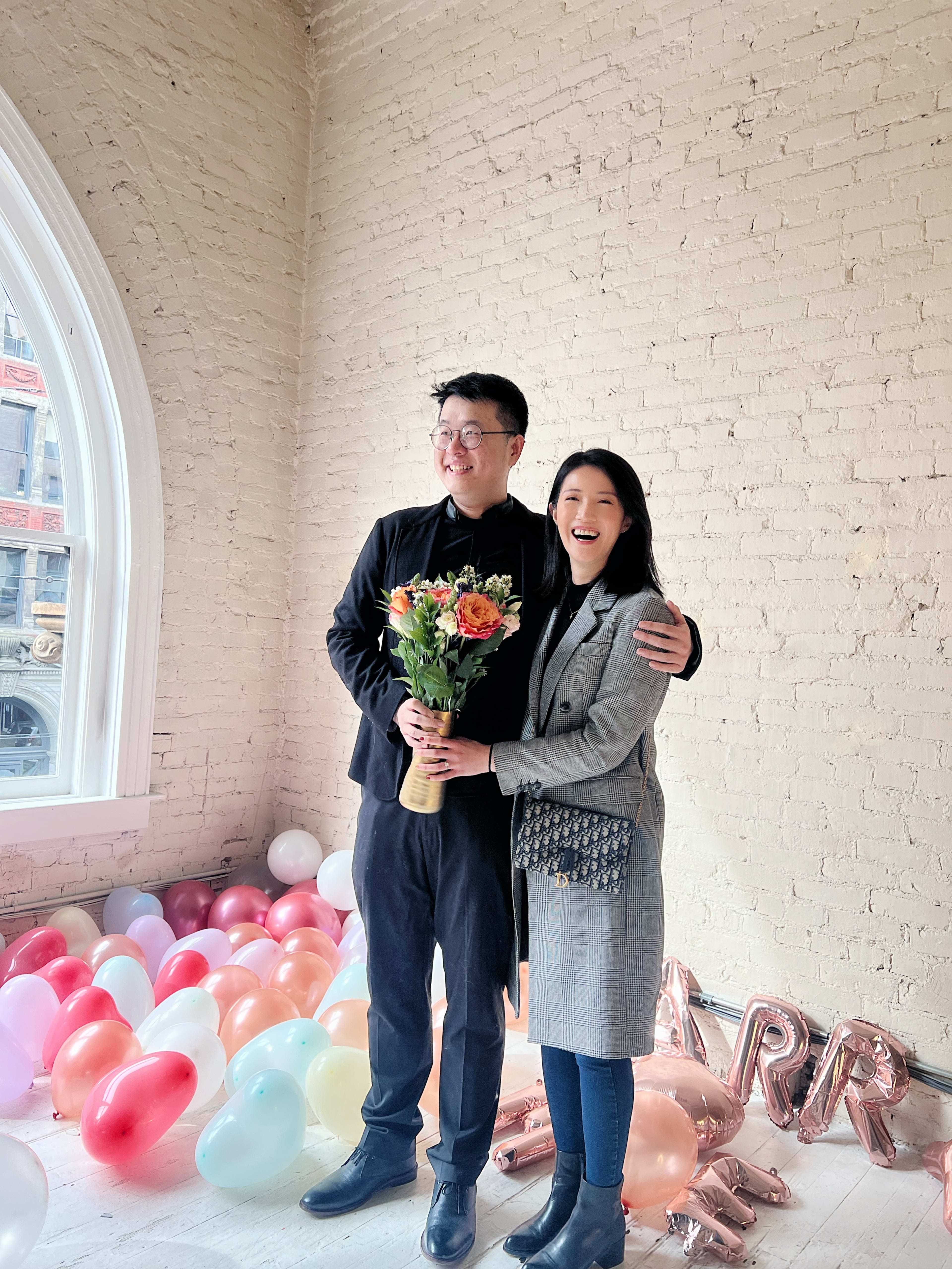 Ein Mann und eine Frau stehen nebeneinander vor Luftballons auf einer Verlobungsfeier.