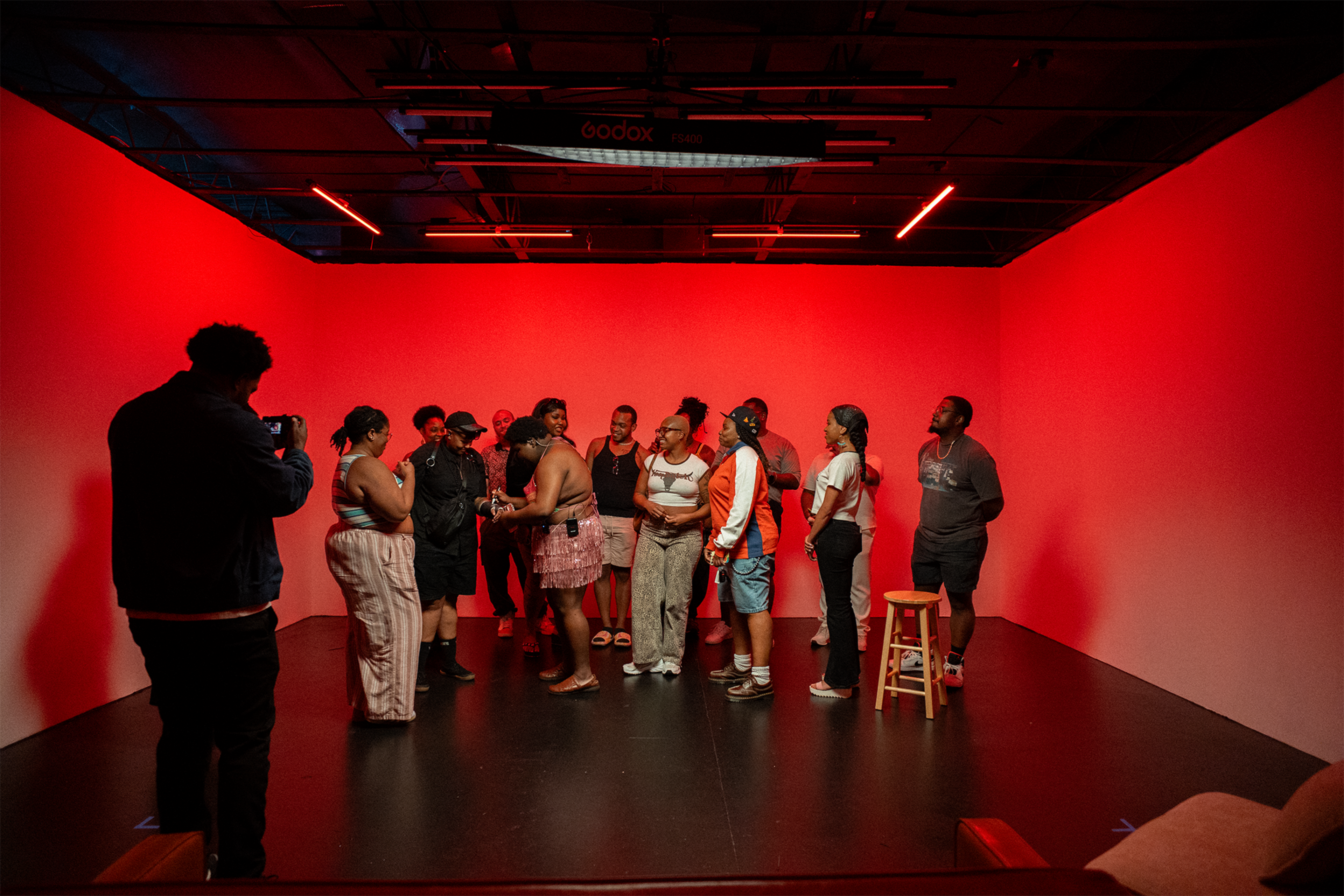 A group of people is gathered in a red-lit studio space for a discussion or activity.