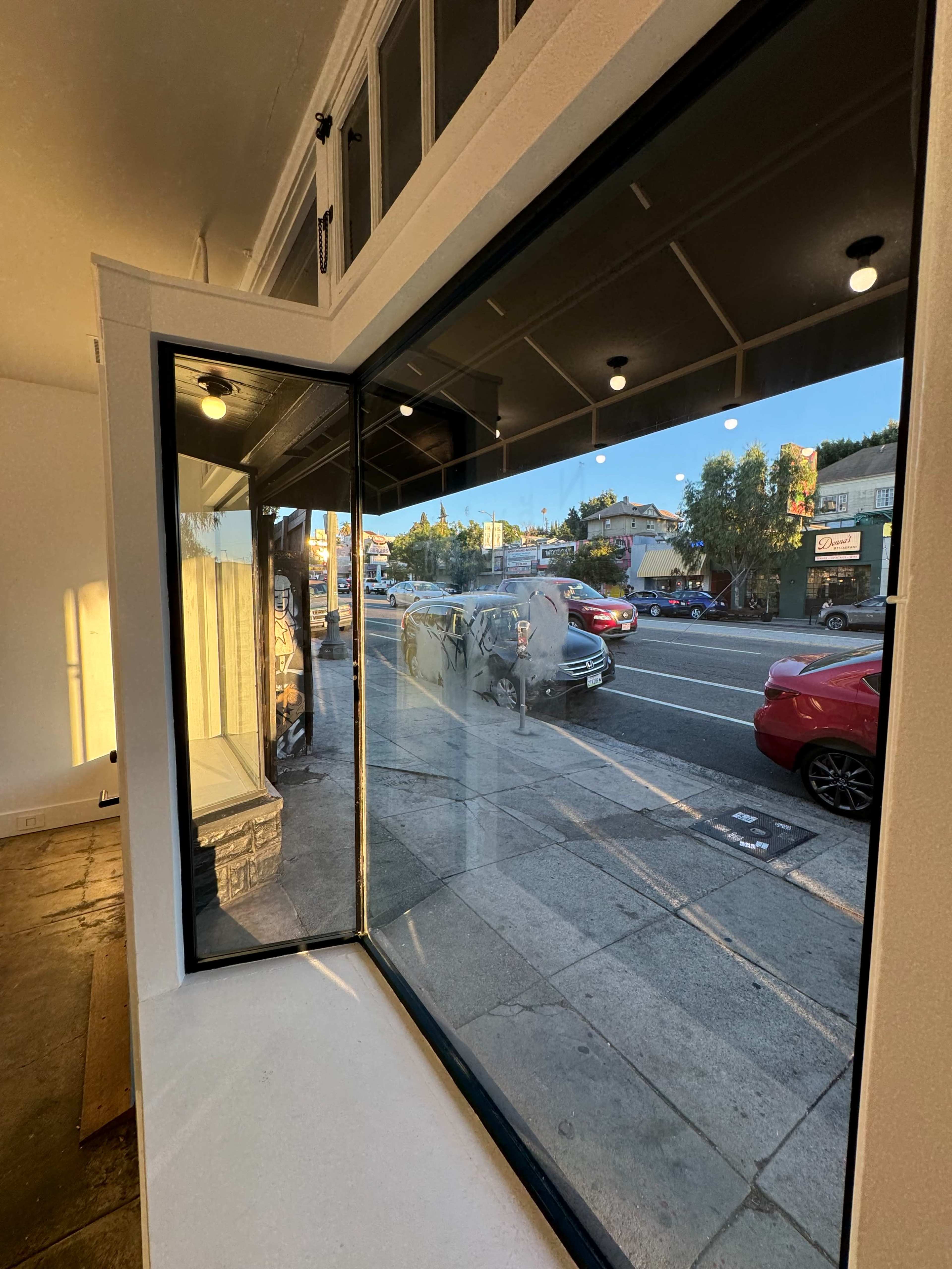 The image shows a large window with a view of a street filled with parked and moving cars, illuminated by the late afternoon sun.
