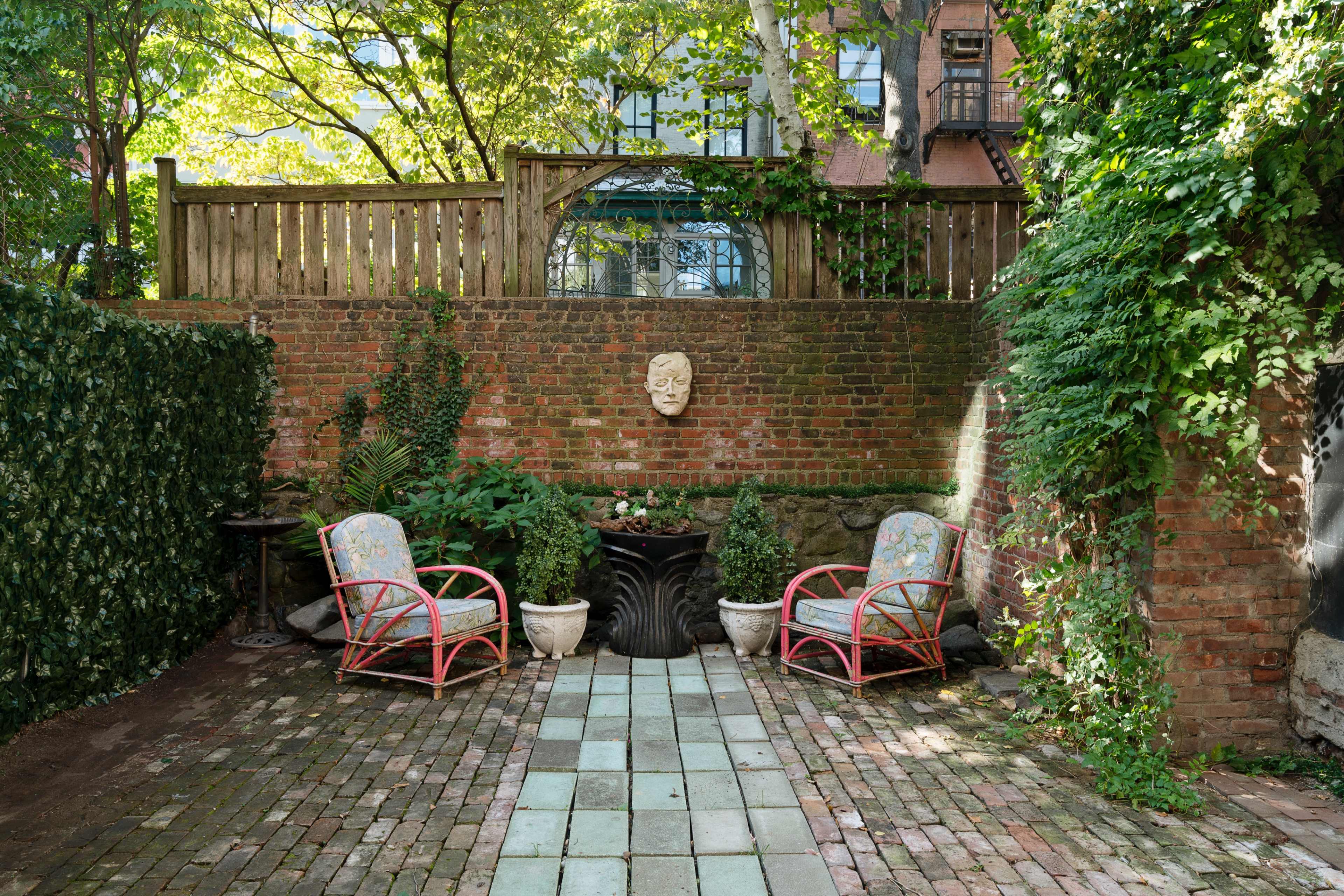 A garden courtyard with two patterned chairs facing a stone planter surrounded by brick walls and greenery.