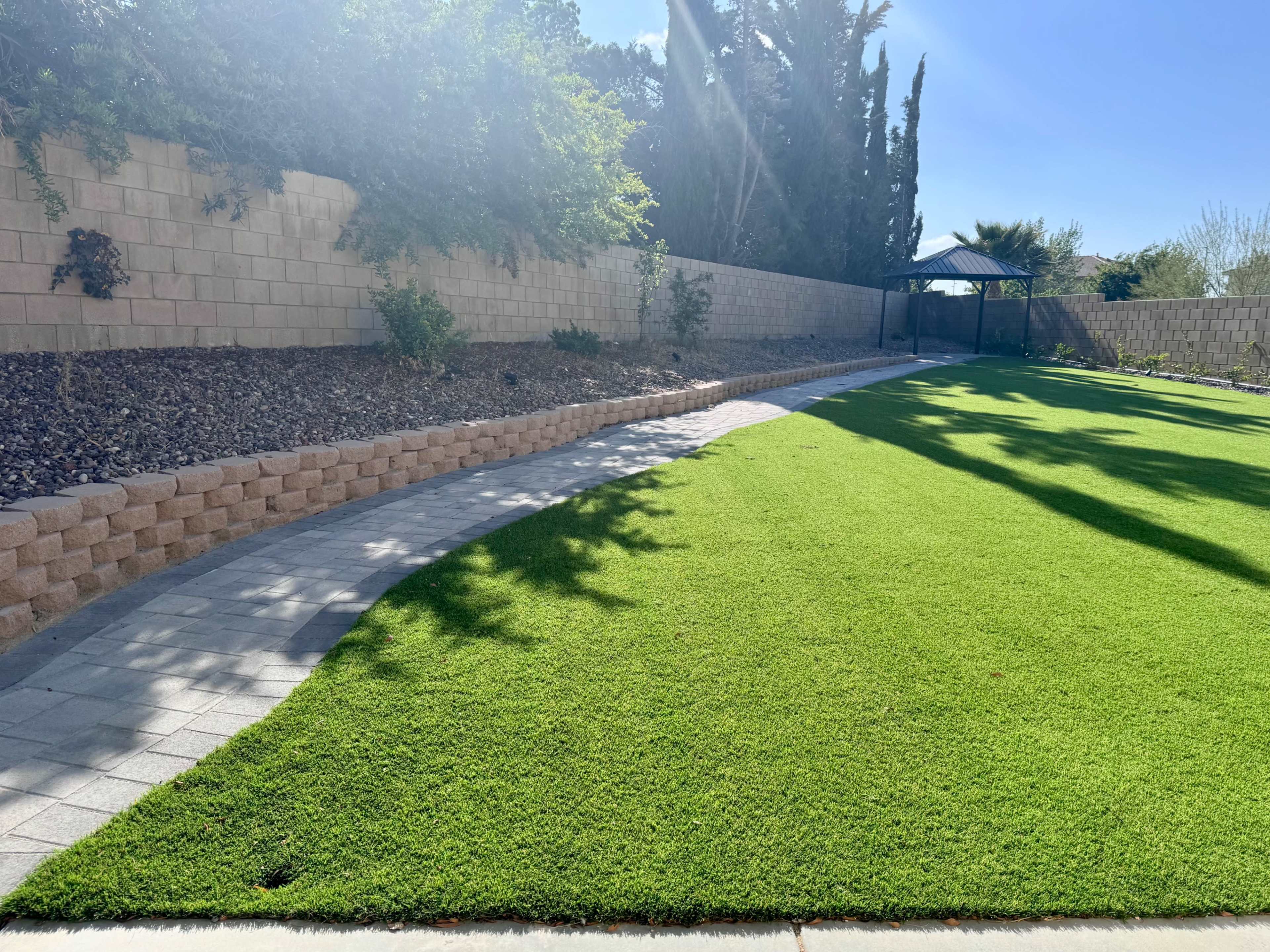A well-maintained backyard with a curved stone pathway bordered by green grass and a wall in the background.