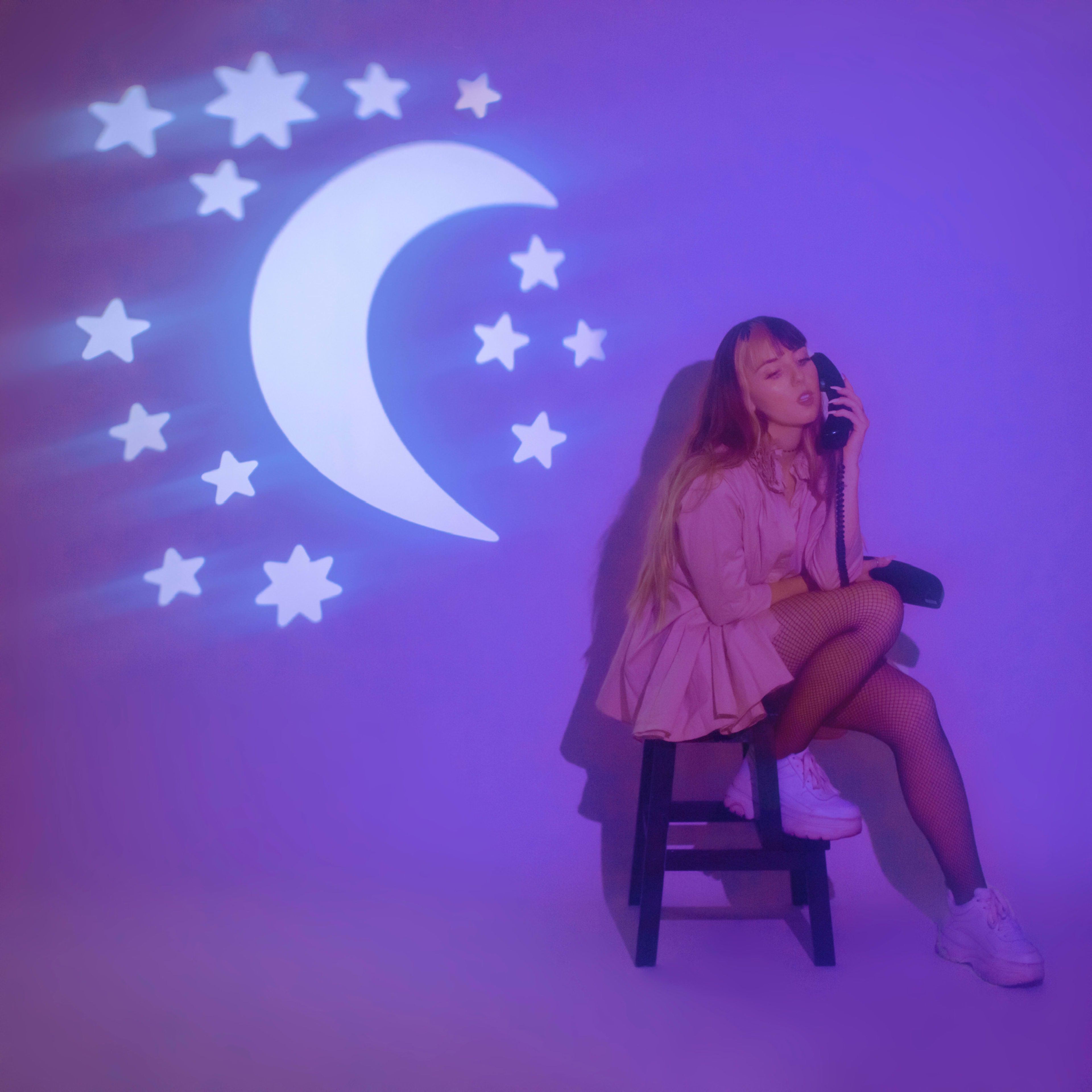 A woman posing for a photoshoot on a chair against a purple backdrop.