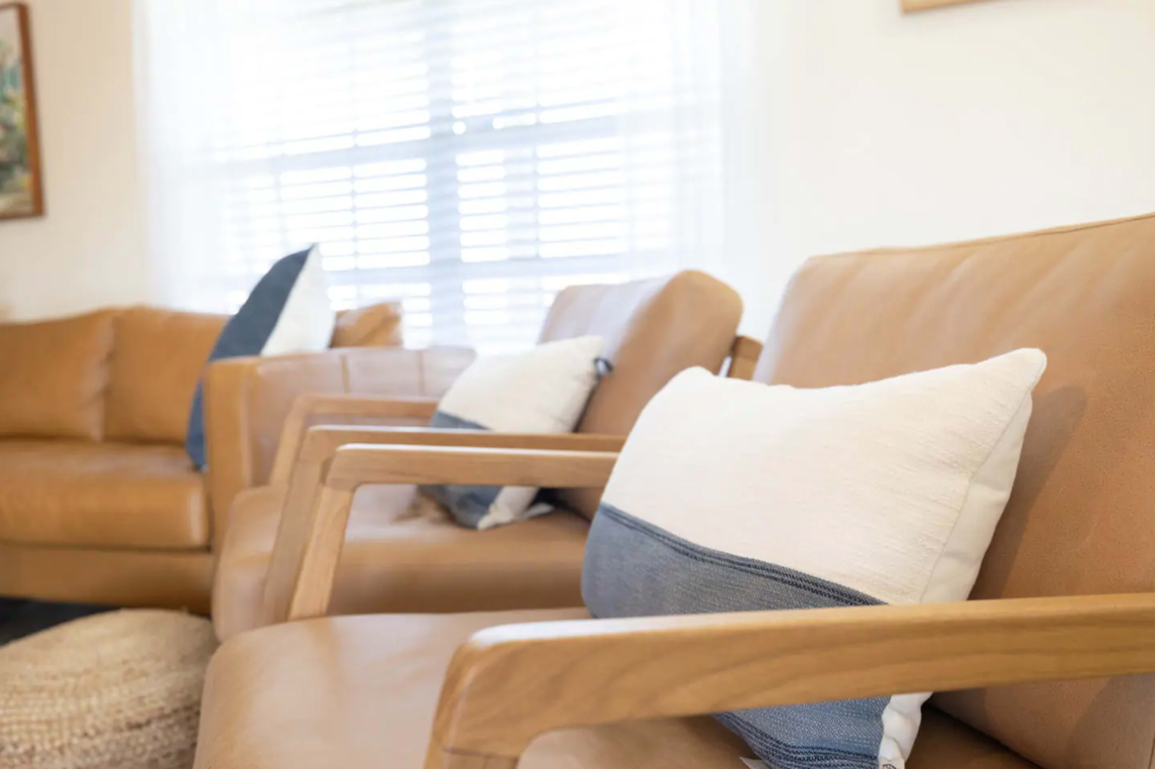 The image shows a living room with two leather chairs featuring blue and white pillows, and a large sofa in the background.