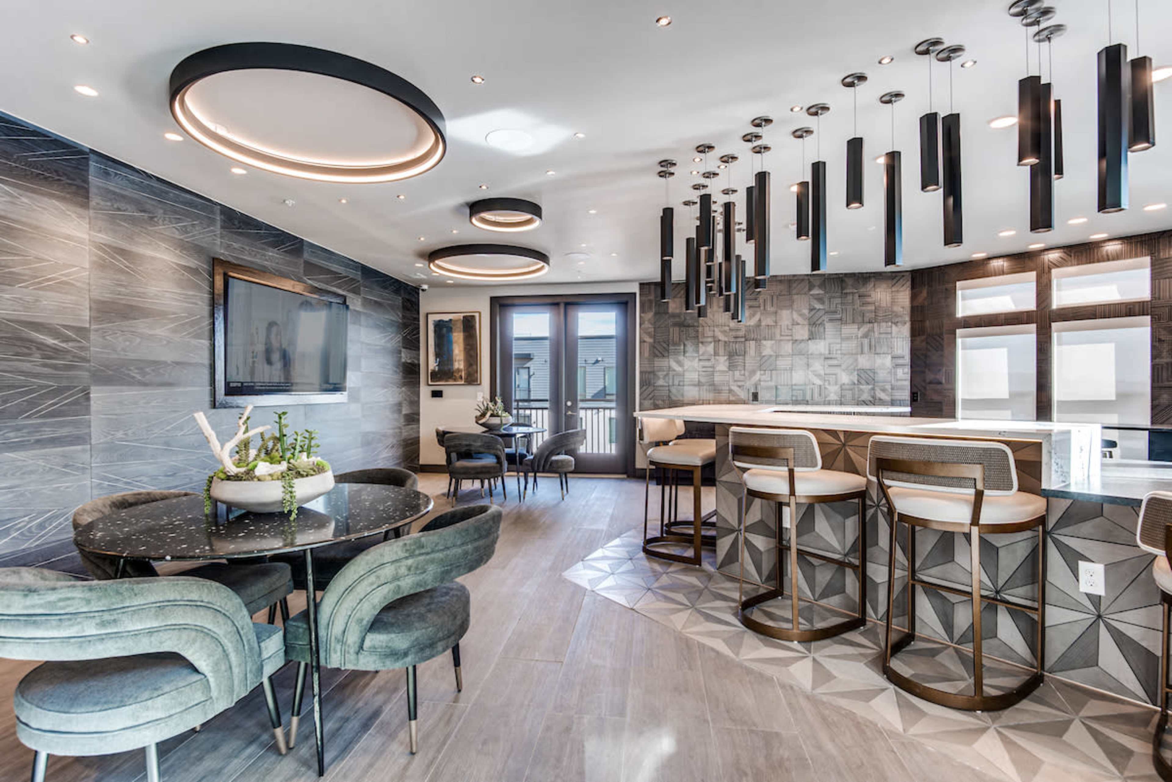 A modern kitchen and dining area with circular light fixtures, a round dining table, and bar seating along a sleek countertop.