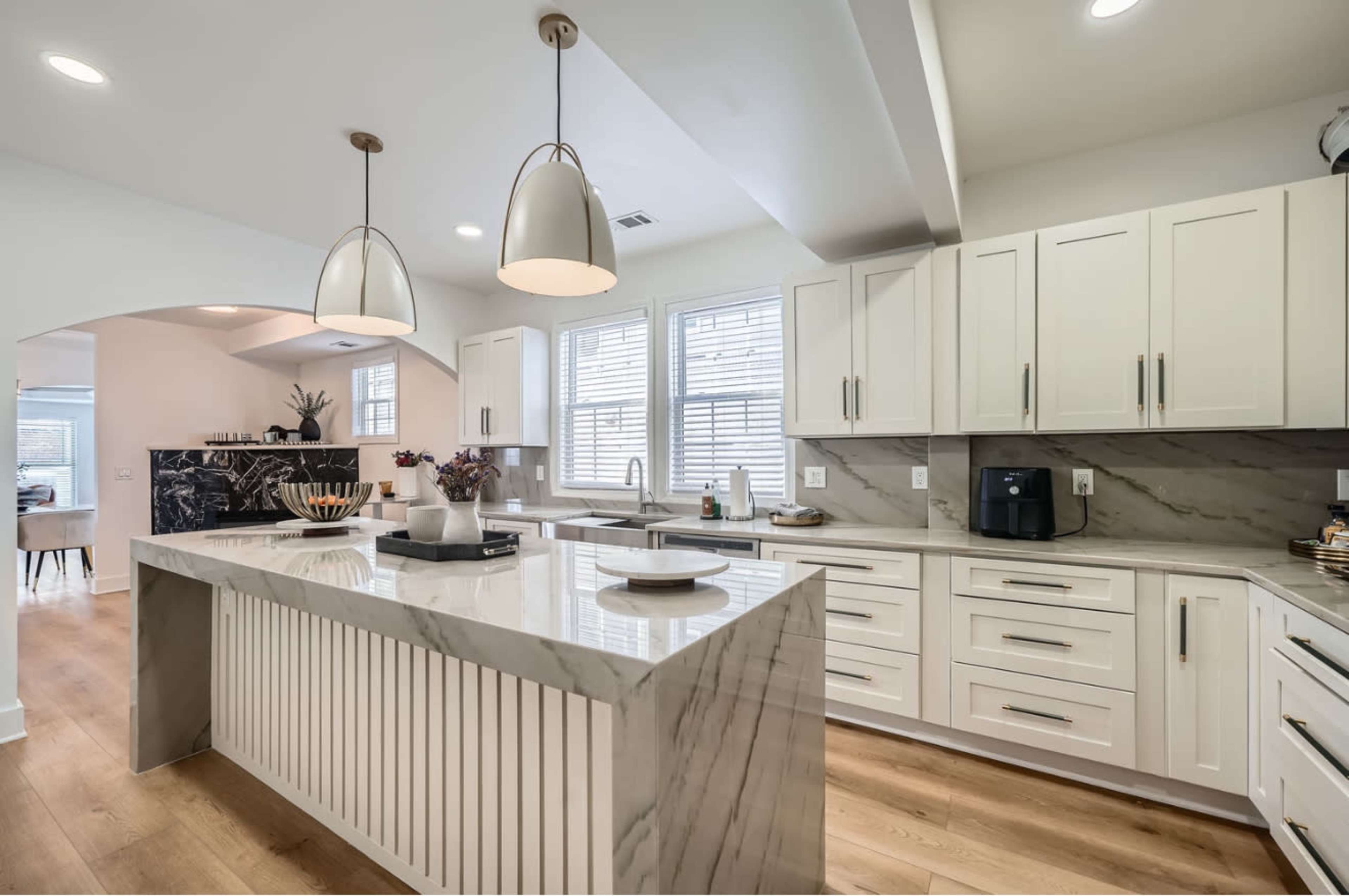 The image shows a modern kitchen featuring a marble island, white cabinetry, and pendant lighting.
