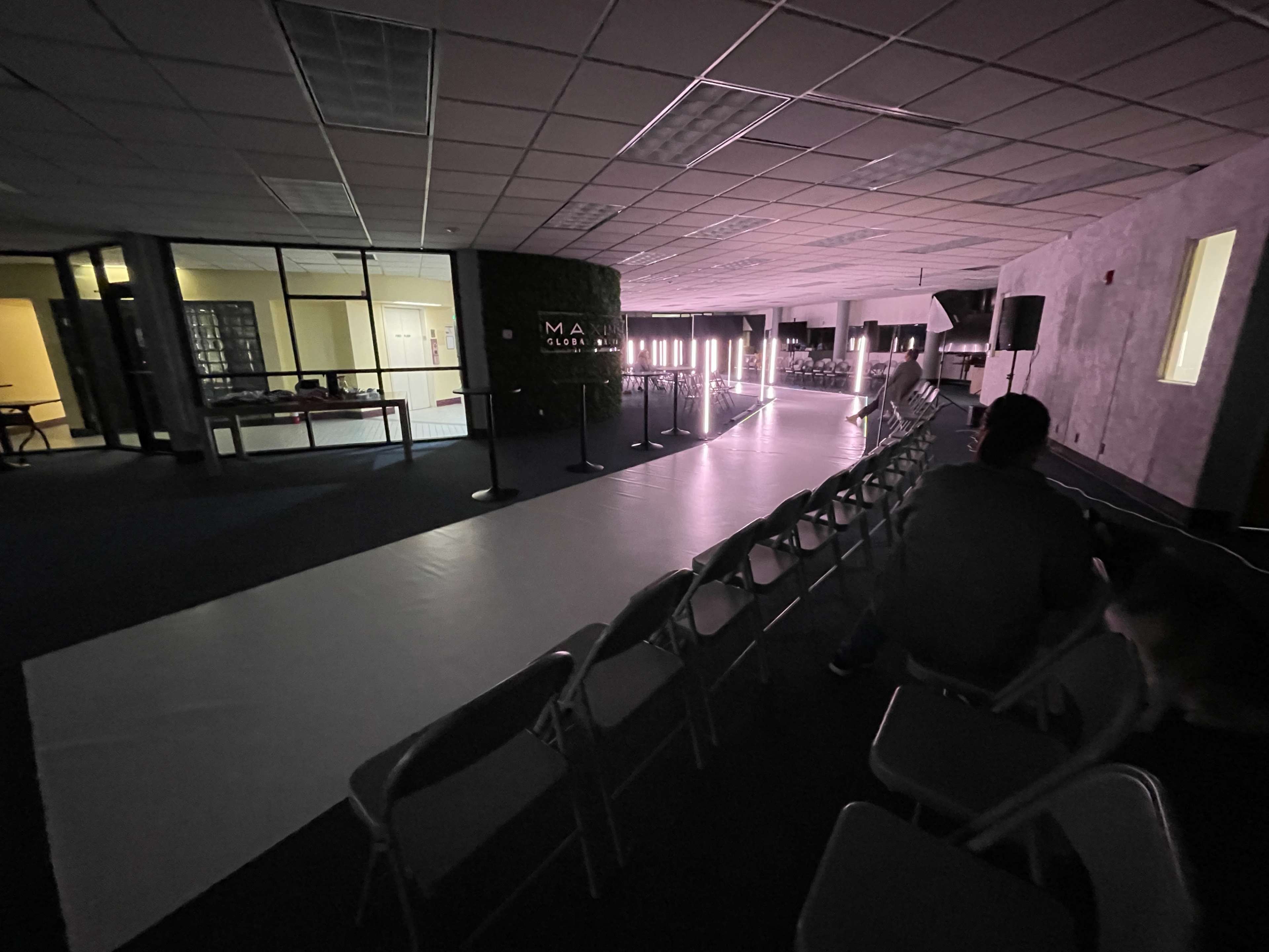 An empty event space with a long runway, chairs arranged for an audience, and soft lighting illuminating the area.