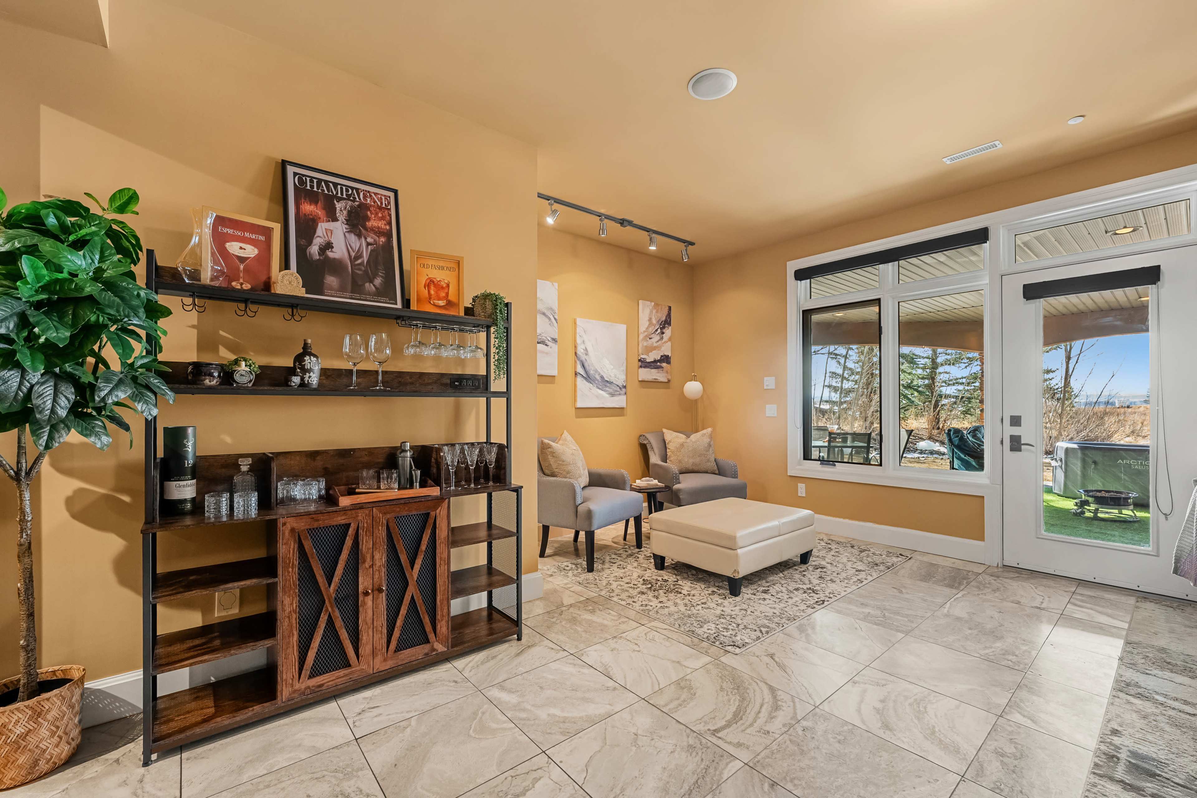 The image shows a cozy indoor space featuring a small seating area with two chairs, a coffee table, and a decorative shelving unit against a warm-toned wall.