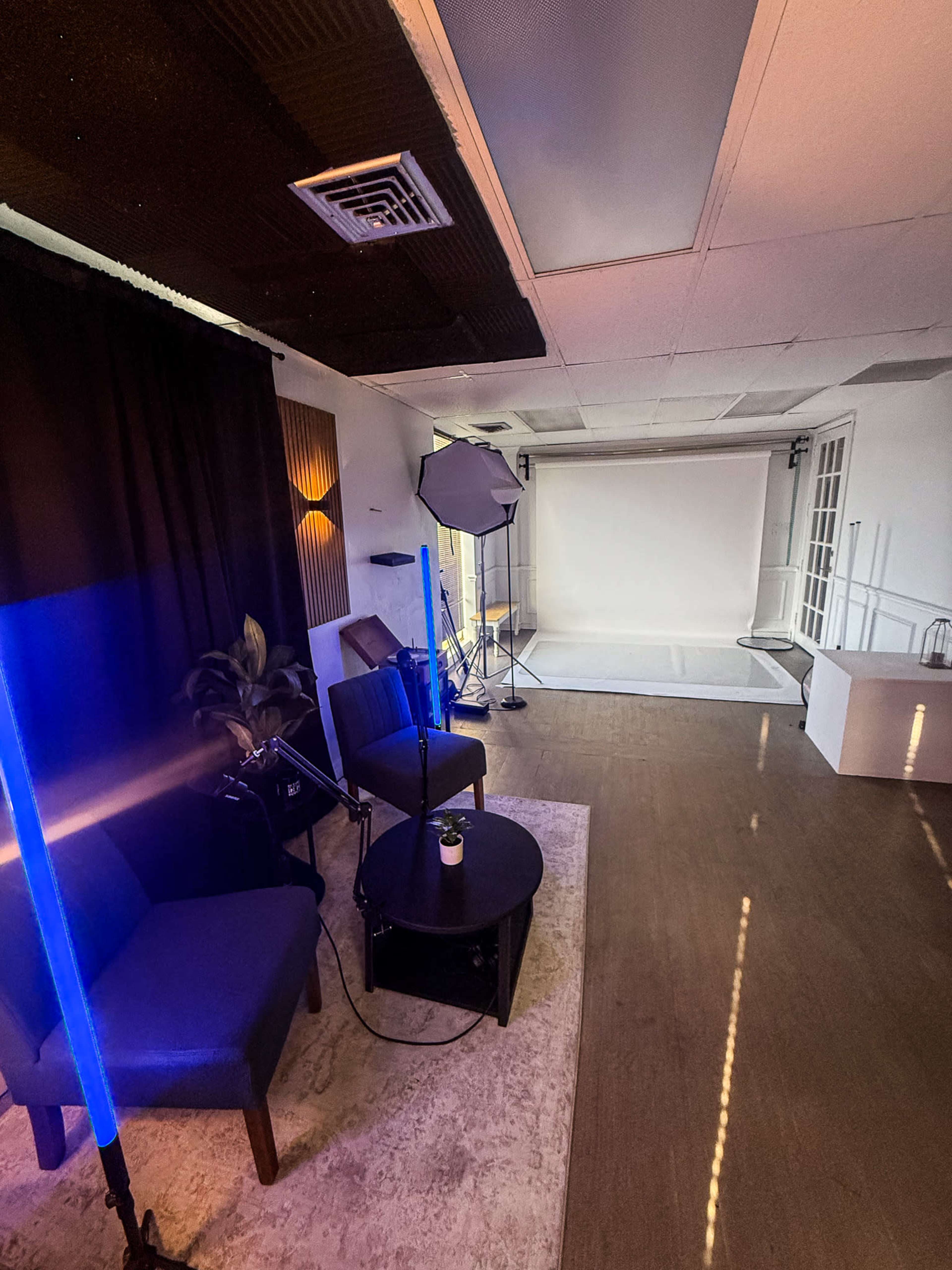The image shows a small studio space with two blue-lit chairs, a black coffee table, and a backdrop set up for photography or videography.