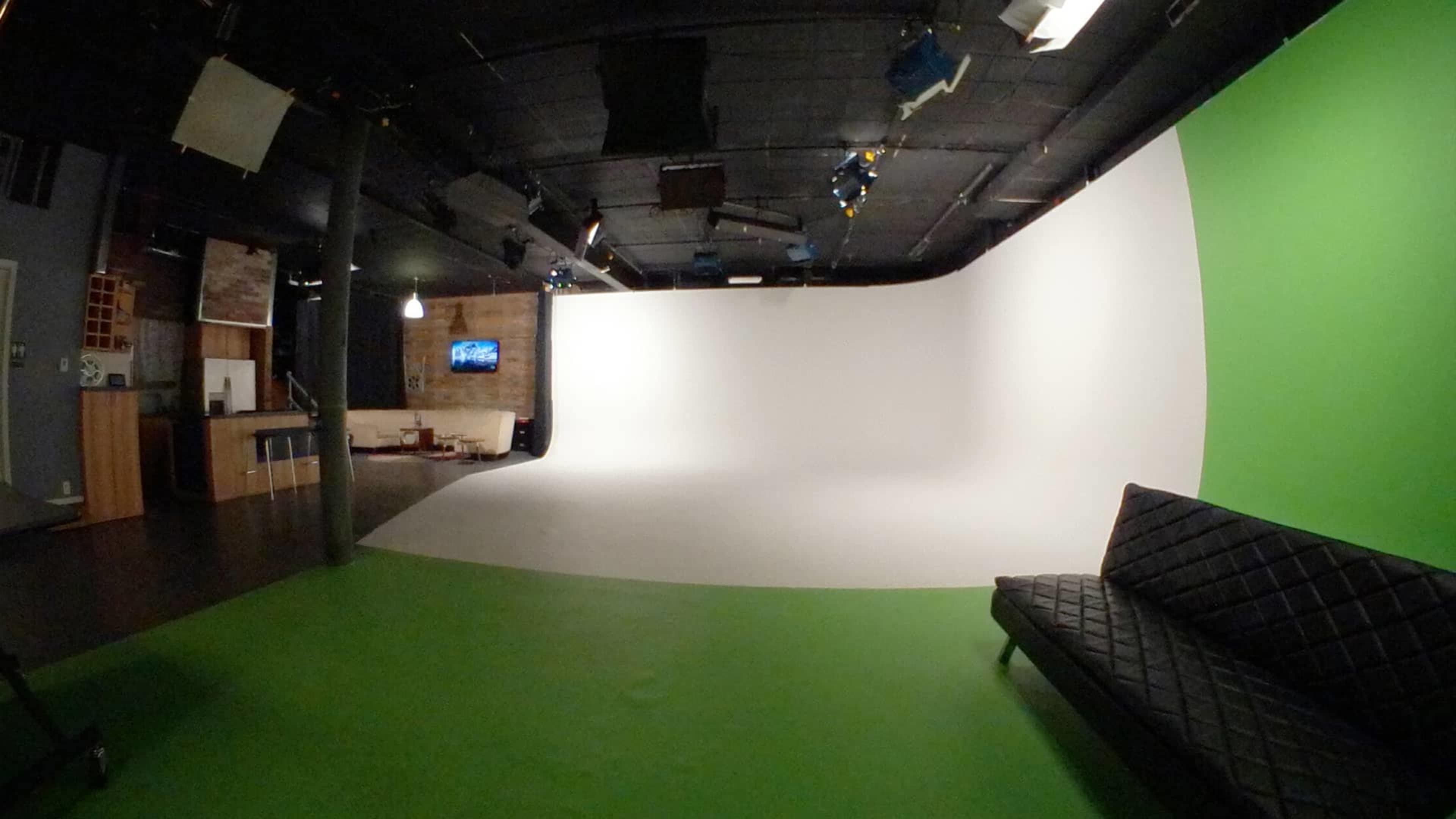 A studio space featuring a green floor, a white backdrop, and a black couch in the foreground.
