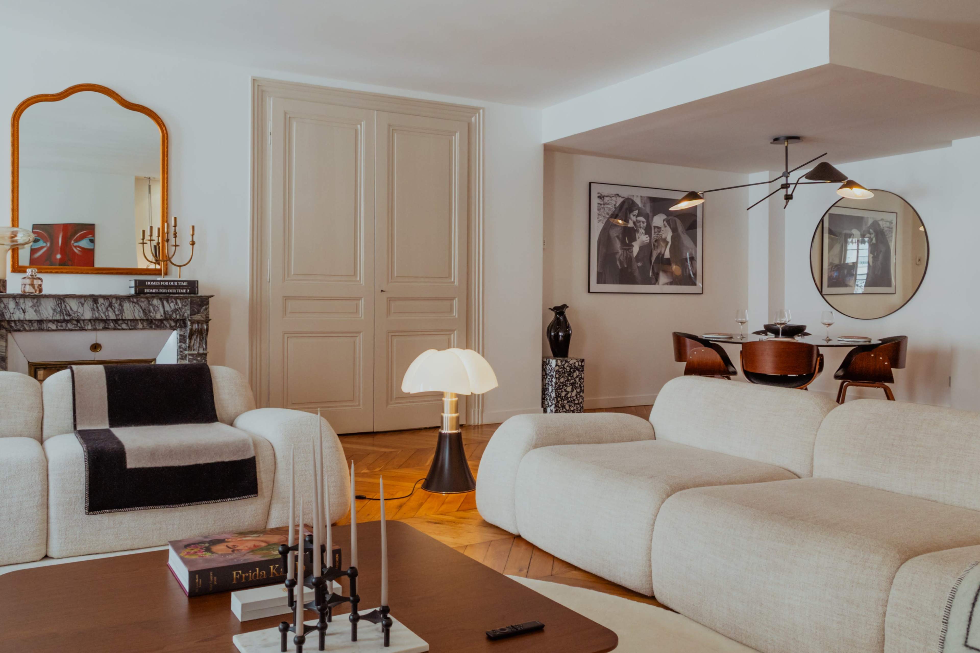 A spacious living room features contemporary furniture, a marble fireplace, and a dining area with round chairs.