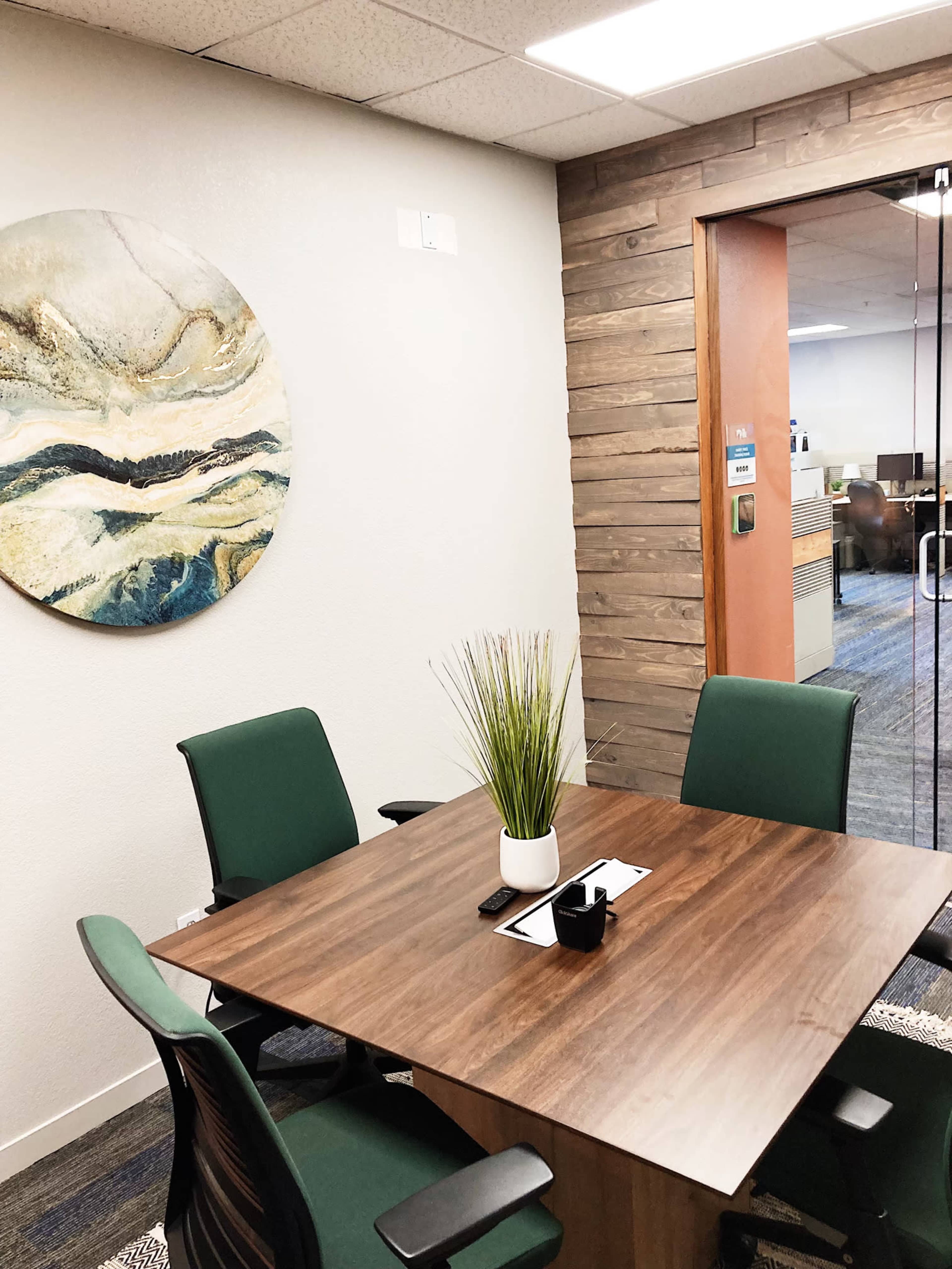 A modern conference room with a wooden table, green chairs, and abstract wall art.
