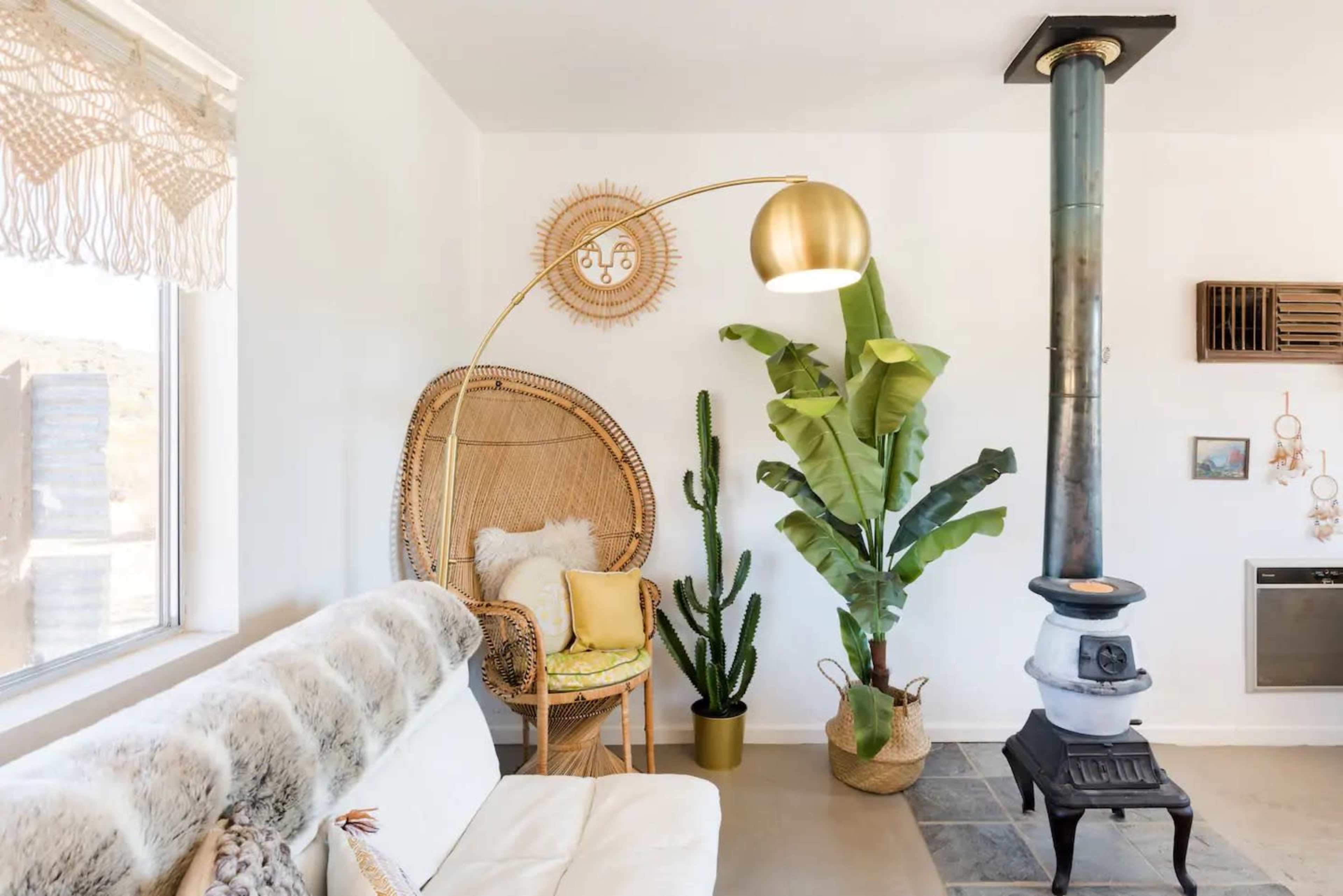 A cozy living space featuring a curved floor lamp, a wicker chair with decorative pillows, a large potted plant, and a cast iron wood stove.