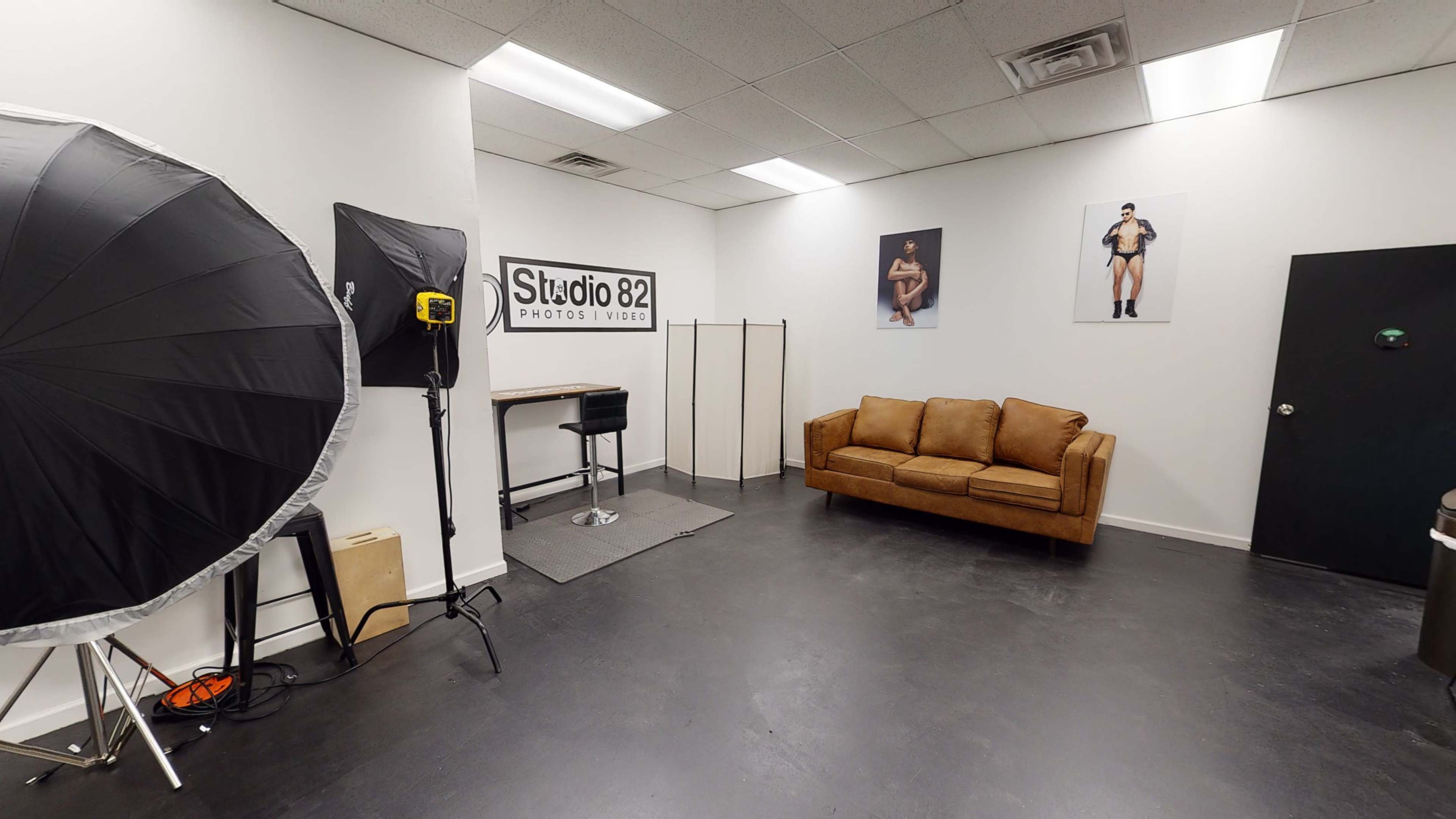 A photography studio with a large softbox light, a brown couch, a work table, and photographs on the walls.