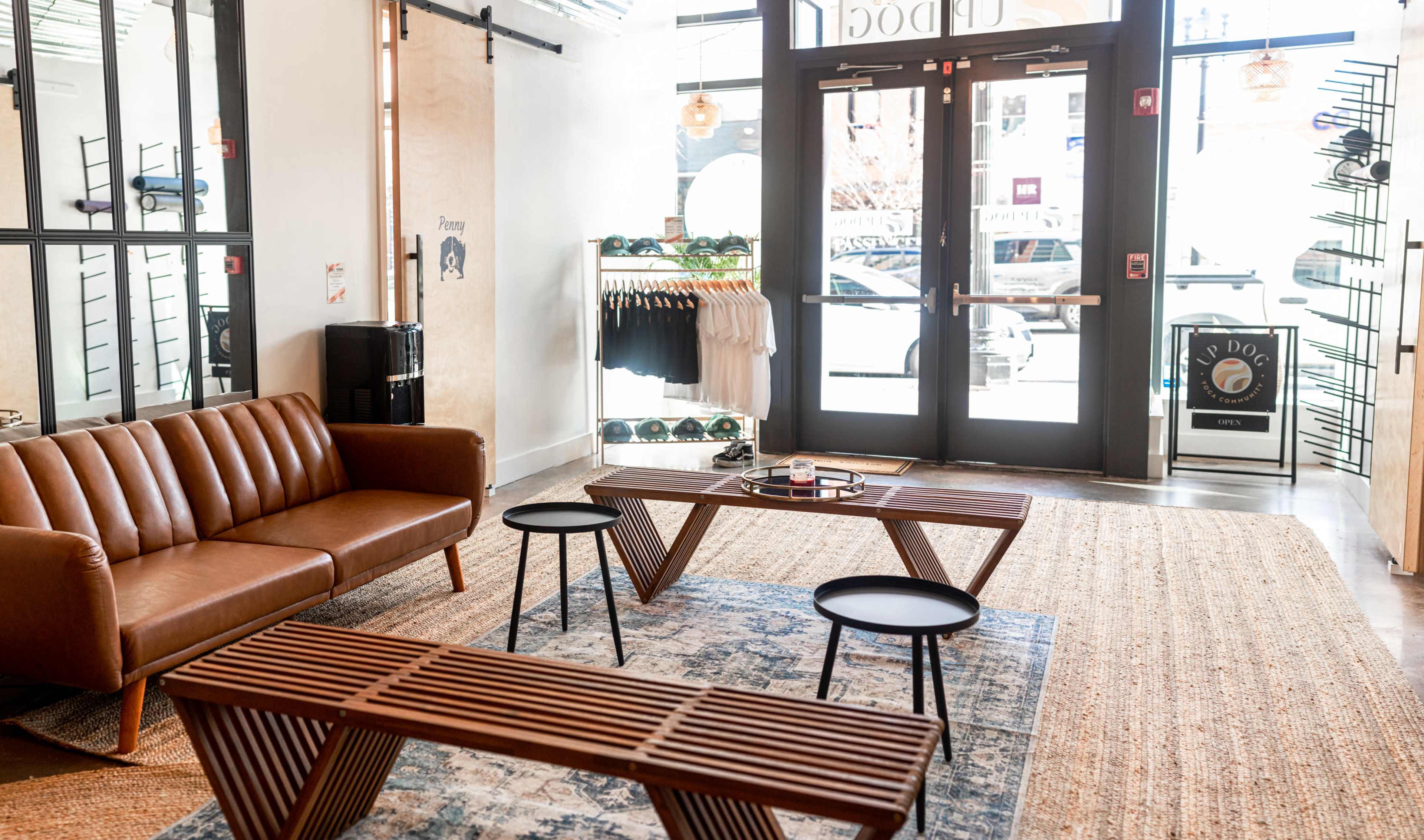 A modern retail space featuring a brown leather sofa, two wooden coffee tables, and displays of clothing and accessories near the entrance.