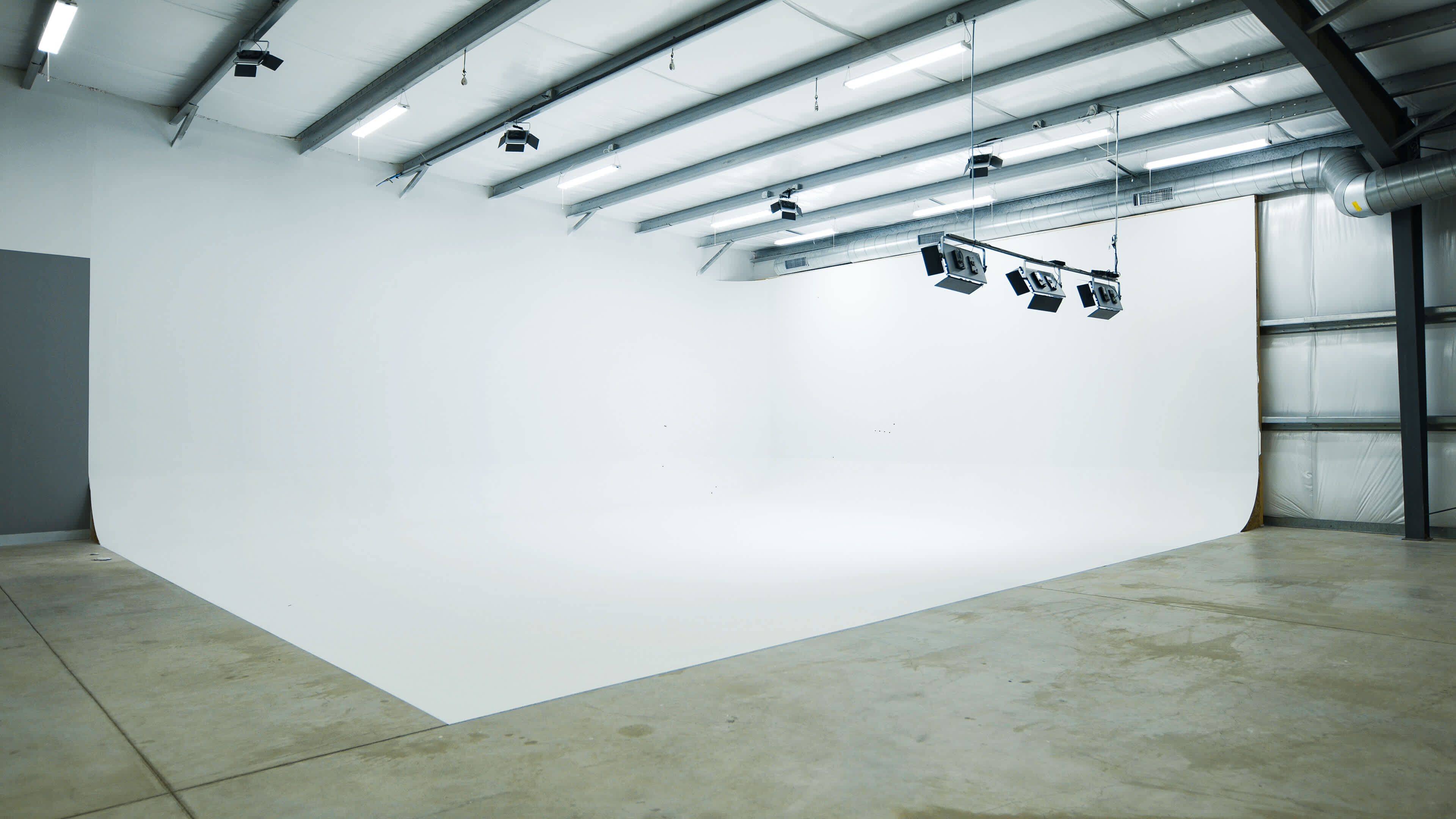 An empty photo studio with a seamless white backdrop and overhead lighting fixtures.