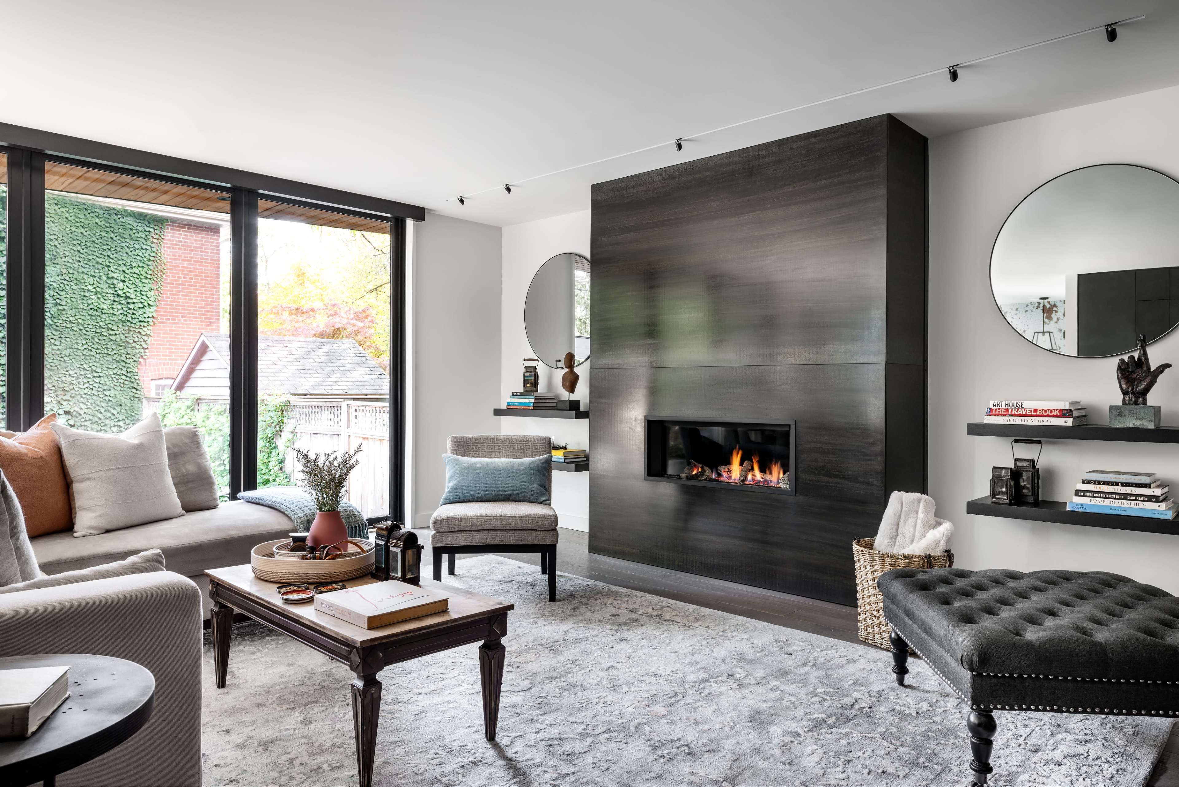 A modern living room features a sleek fireplace on a dark wall, flanked by mirrors, with a cozy seating arrangement and decorative shelves.