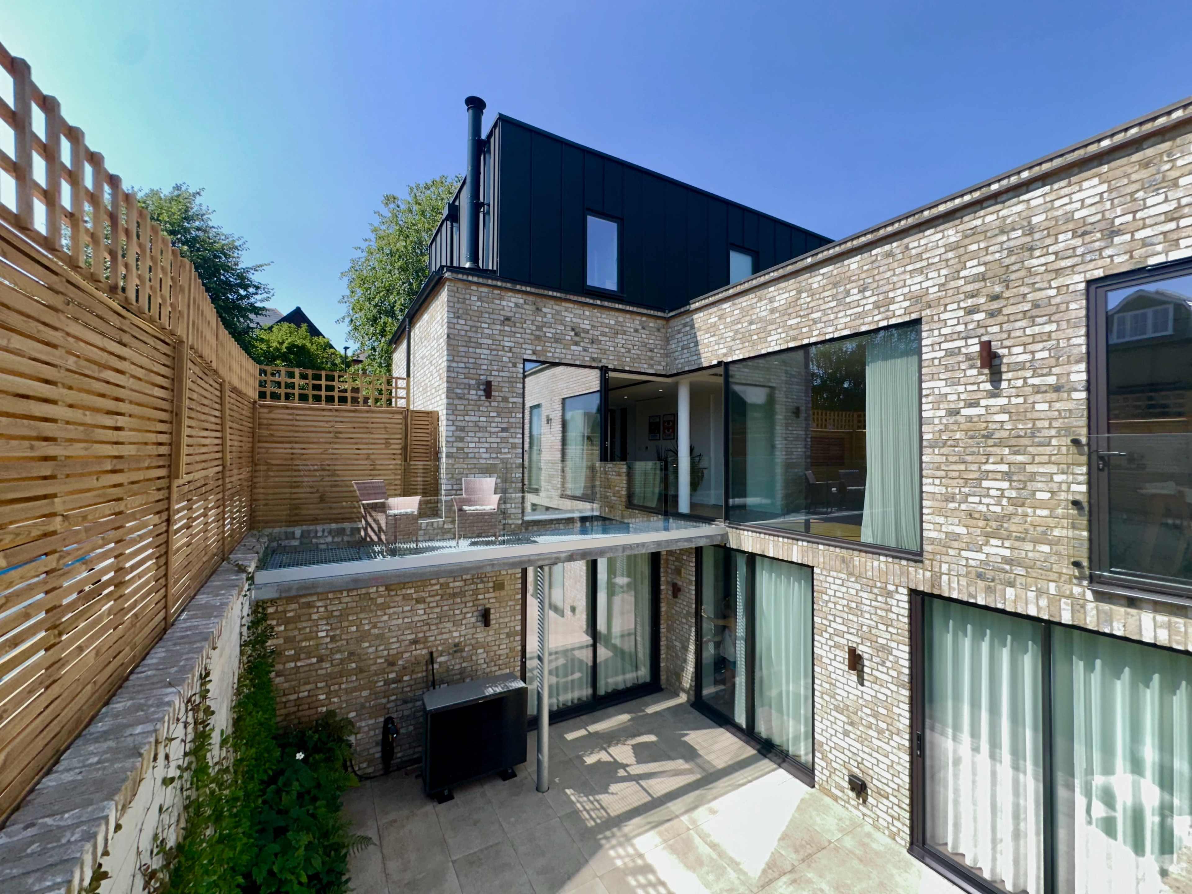 A modern brick house features large glass windows and a terrace surrounded by a wooden fence.