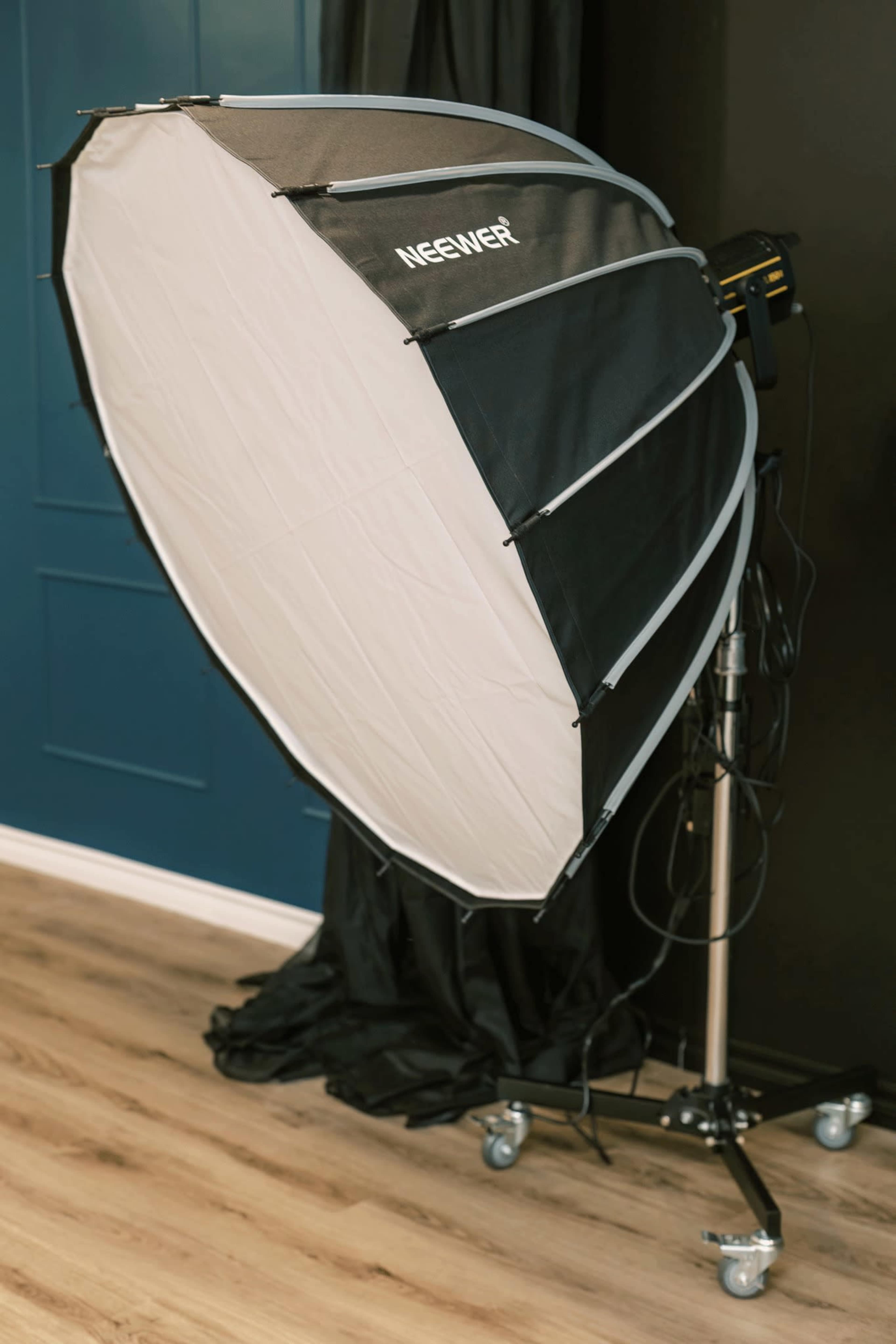 A large softbox light mounted on a mobile stand is positioned against a dark wall in a studio setting.