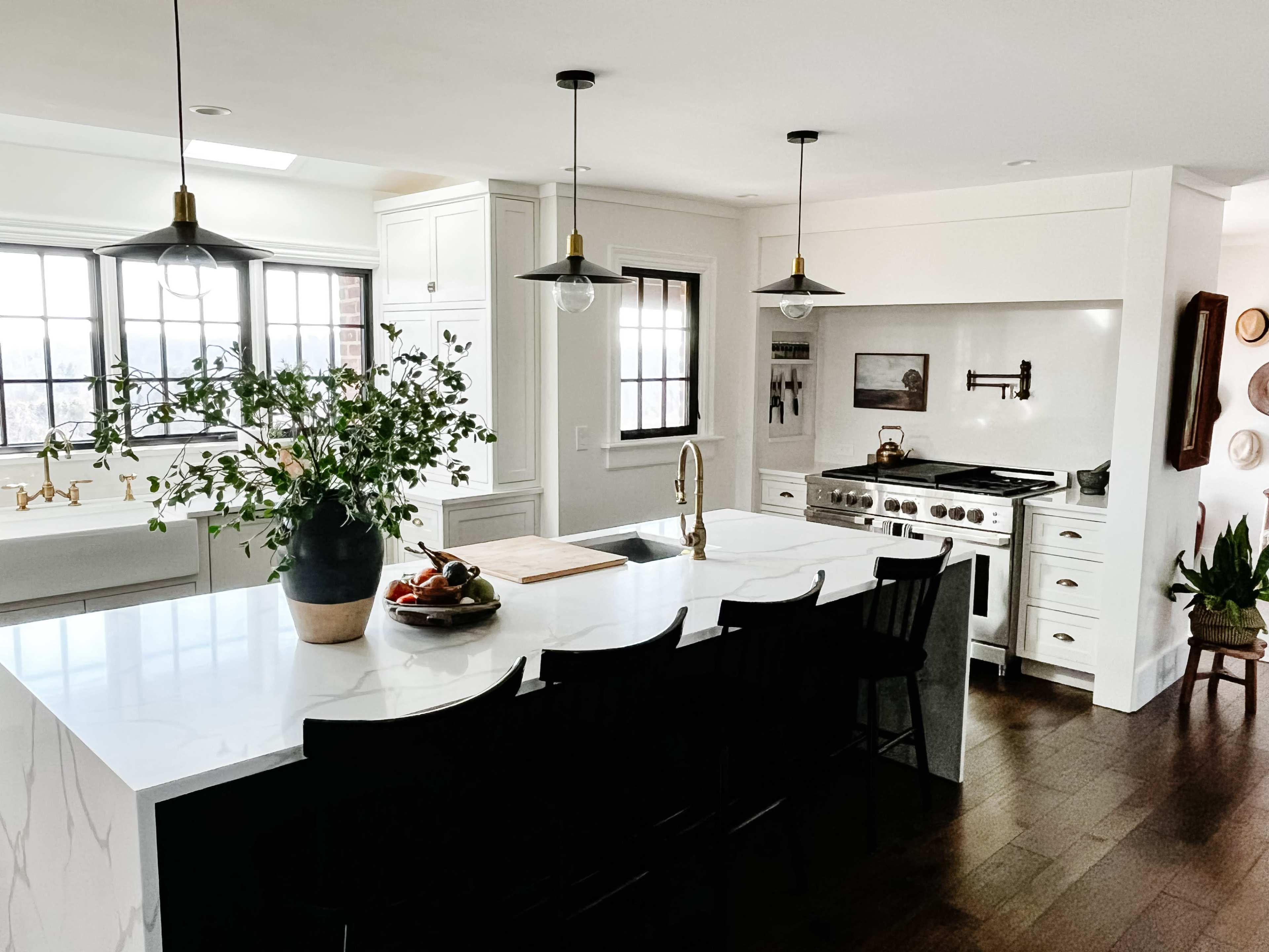 A modern kitchen features a white marble island with a black seating area, a large stove, and natural light from a window.