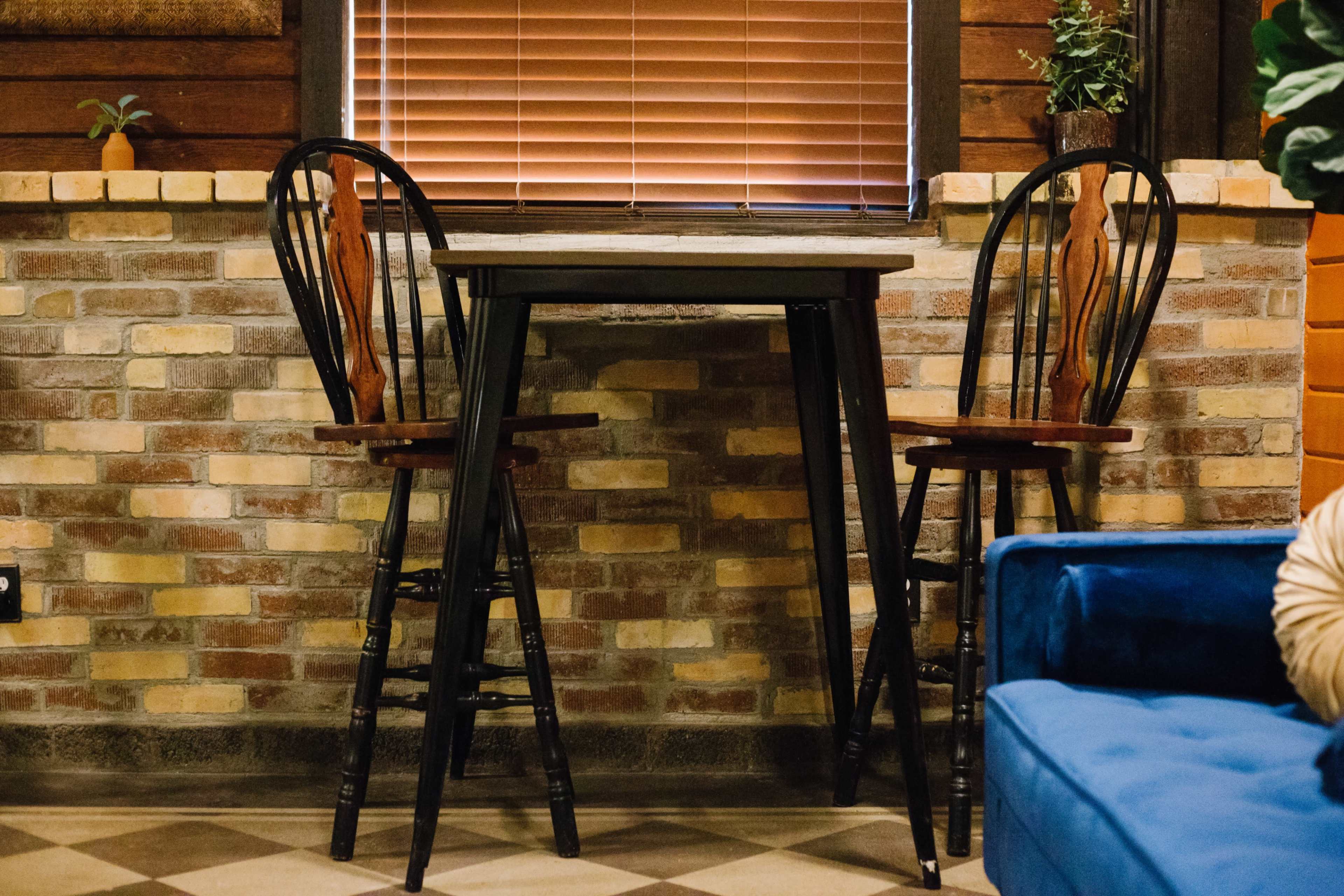 A small, wooden table with two high-backed chairs positionedagainst a brick wall with wooden accents.