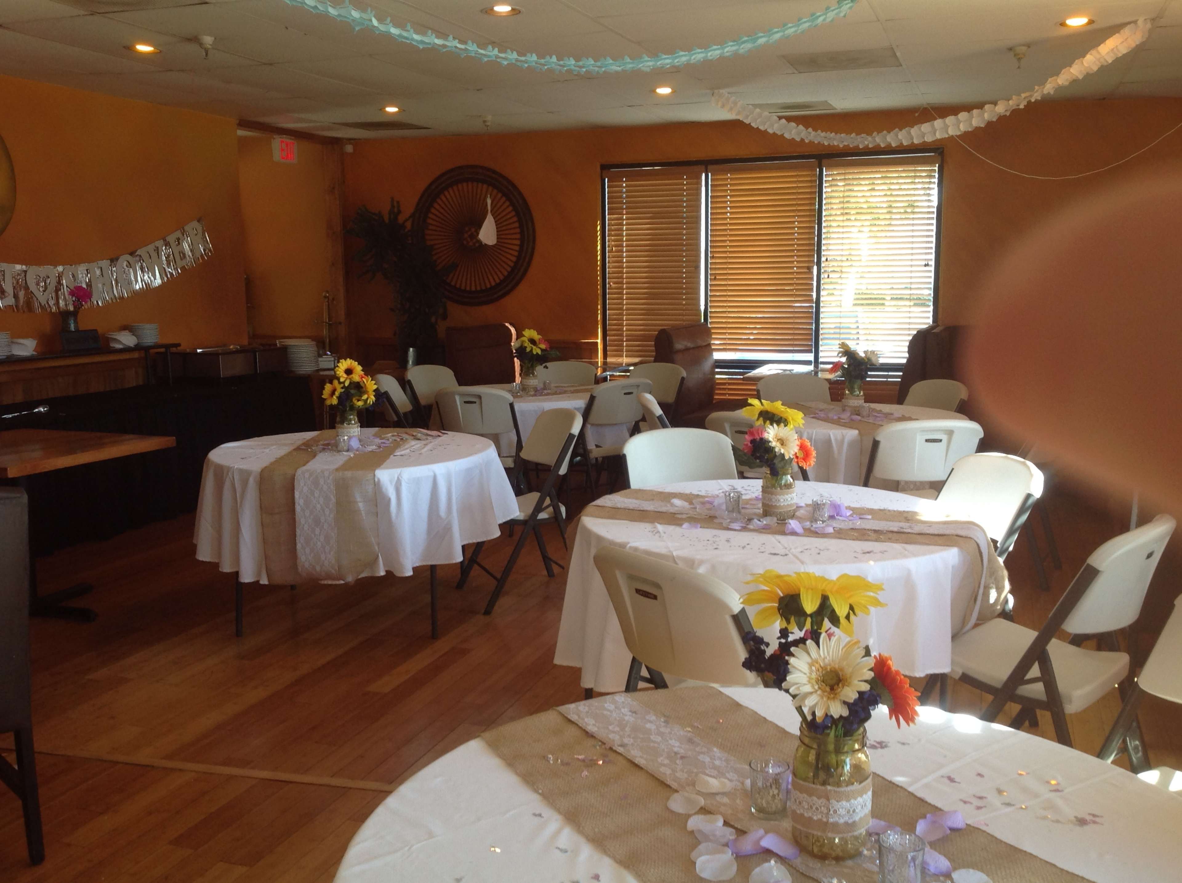 A banquet hall set with several round tables adorned with white tablecloths, centerpieces of flowers, and decorative details.