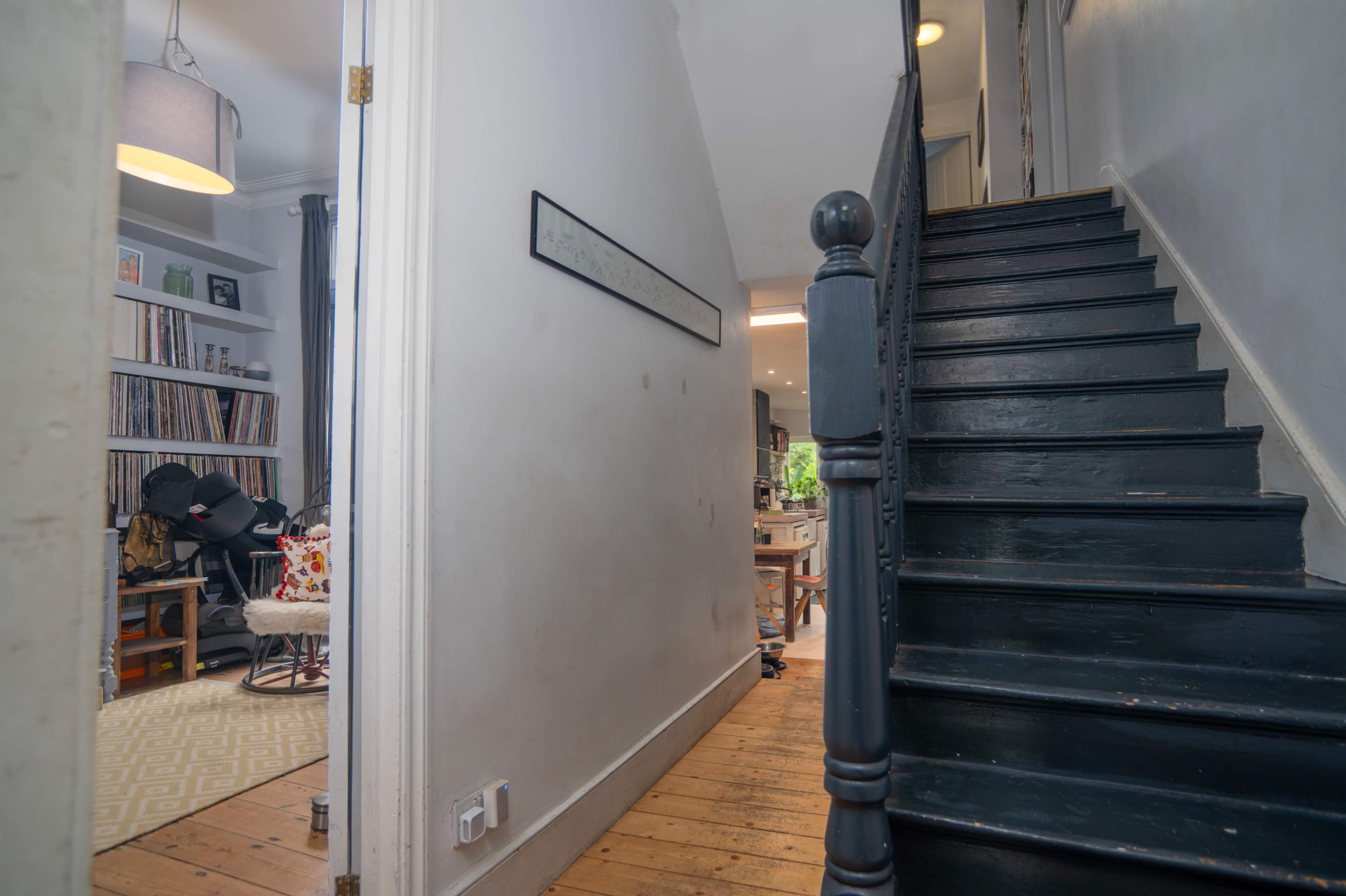 The image shows a hallway with a wooden staircase leading upward, flanked by a partially visible room on the left.