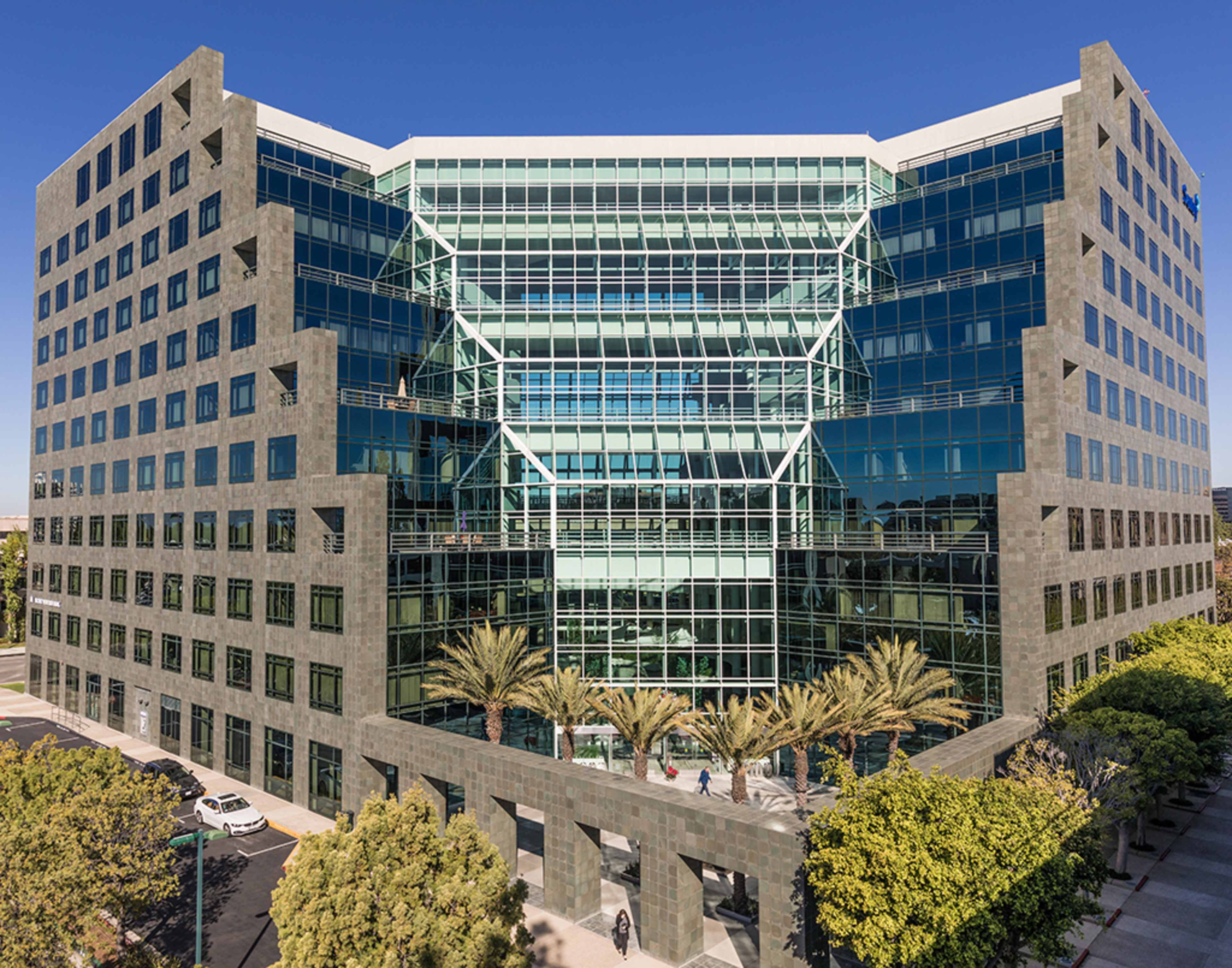 A modern glass office building with multiple stories and palm trees in the foreground.