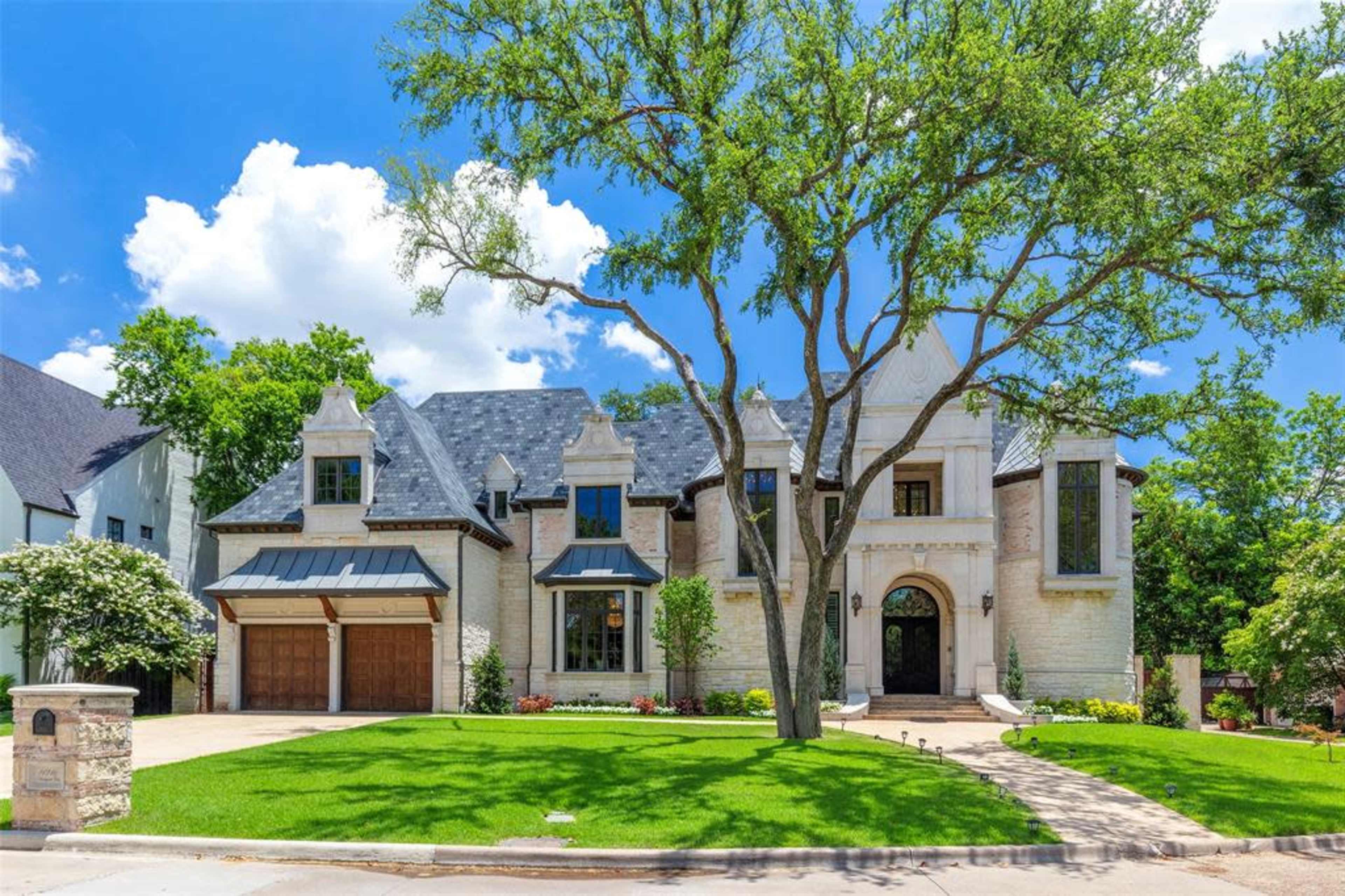 The image shows a large, two-story, stone and brick house with a symmetrical facade, surrounded by well-maintained greenery and a driveway.