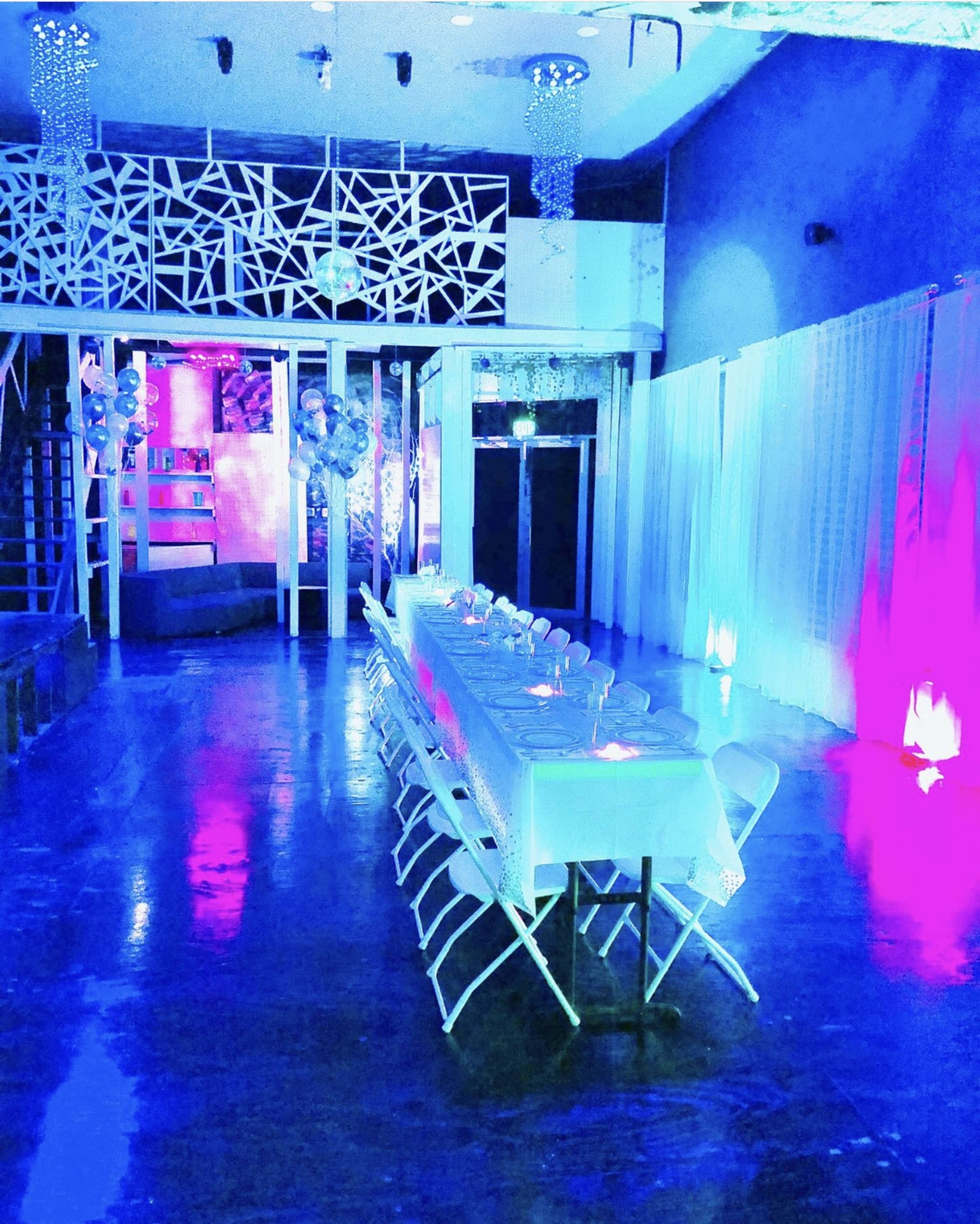 A long, elegantly set table is arranged in a brightly lit event space with colorful lighting and decorative elements.